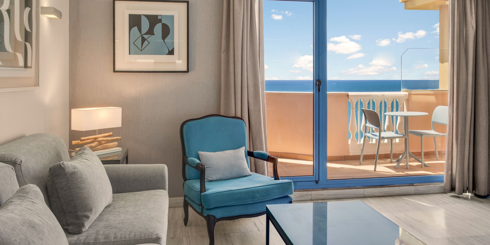 Coastal living room with ocean view balcony, gray sofa, and teal armchair.