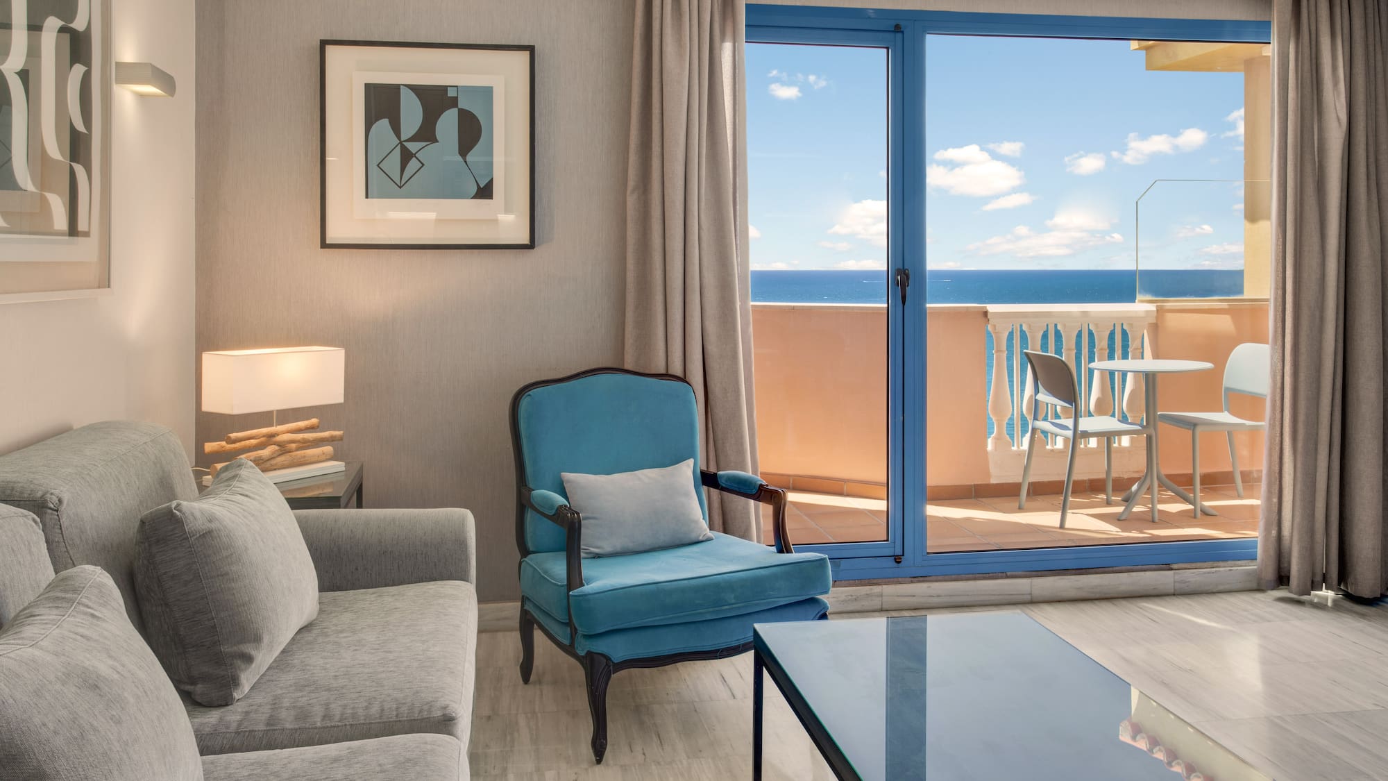 Coastal living room with ocean view balcony, gray sofa, and teal armchair.
