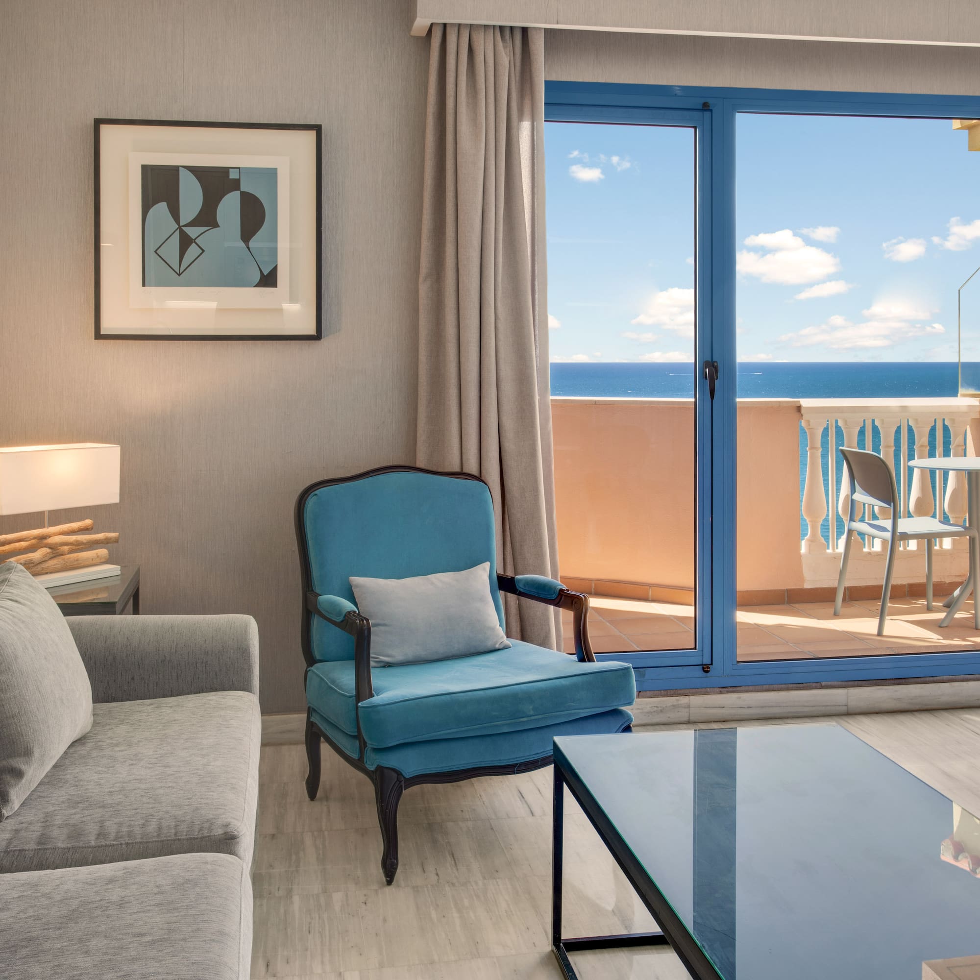 Coastal living room with ocean view balcony, gray sofa, and teal armchair.