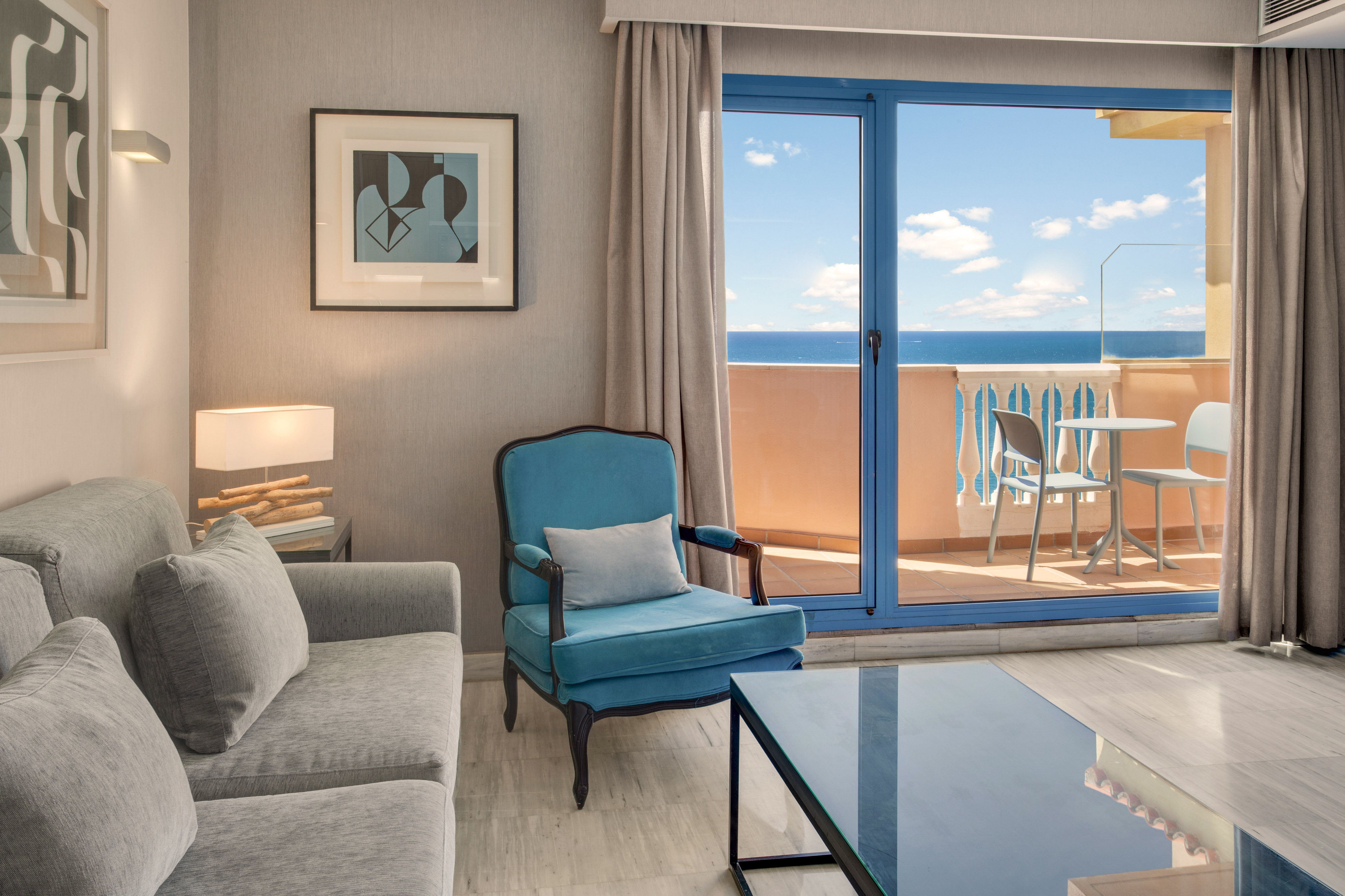 Coastal living room with ocean view balcony, gray sofa, and teal armchair.