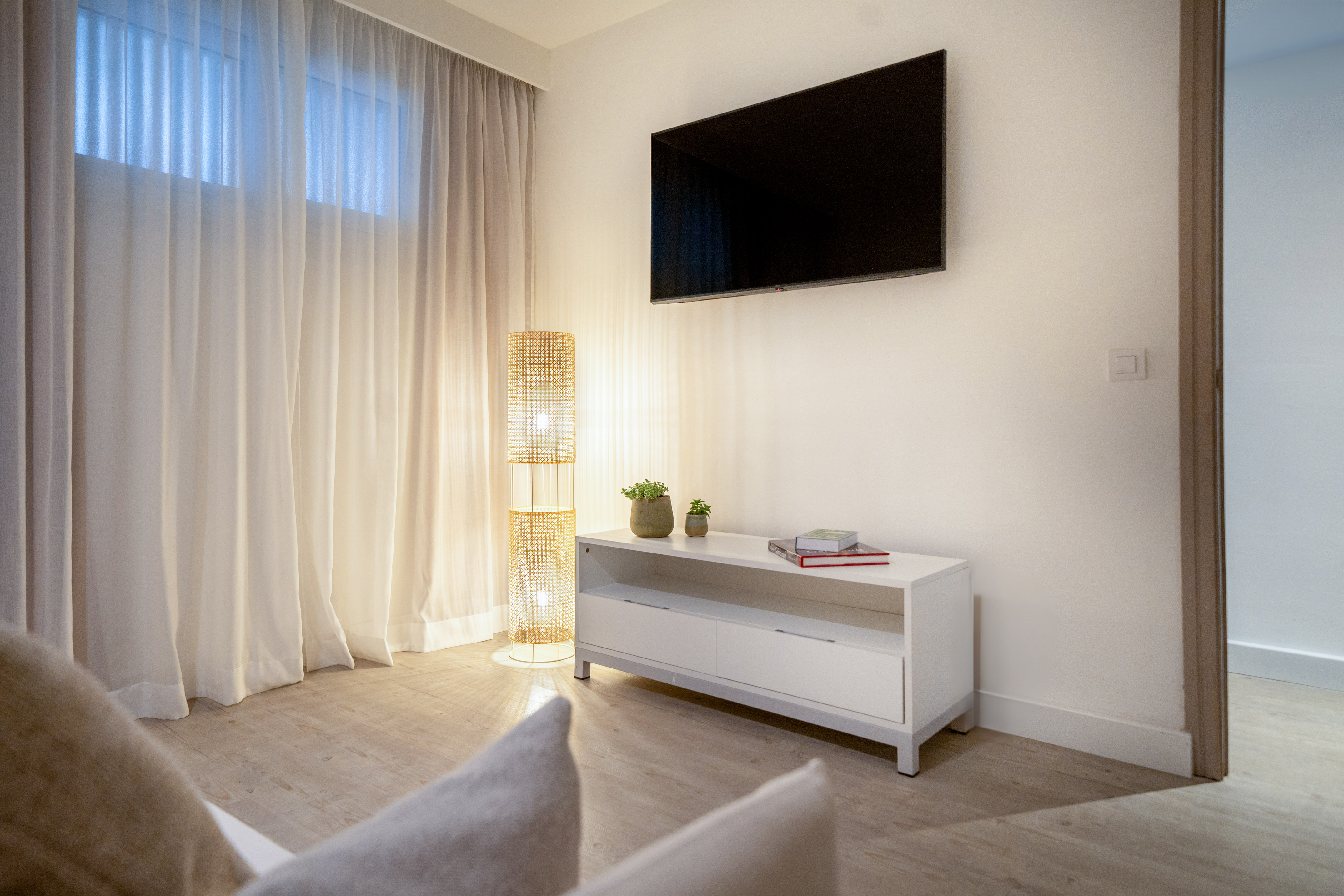Modern living room with wall TV, white media console, and rattan lamp.