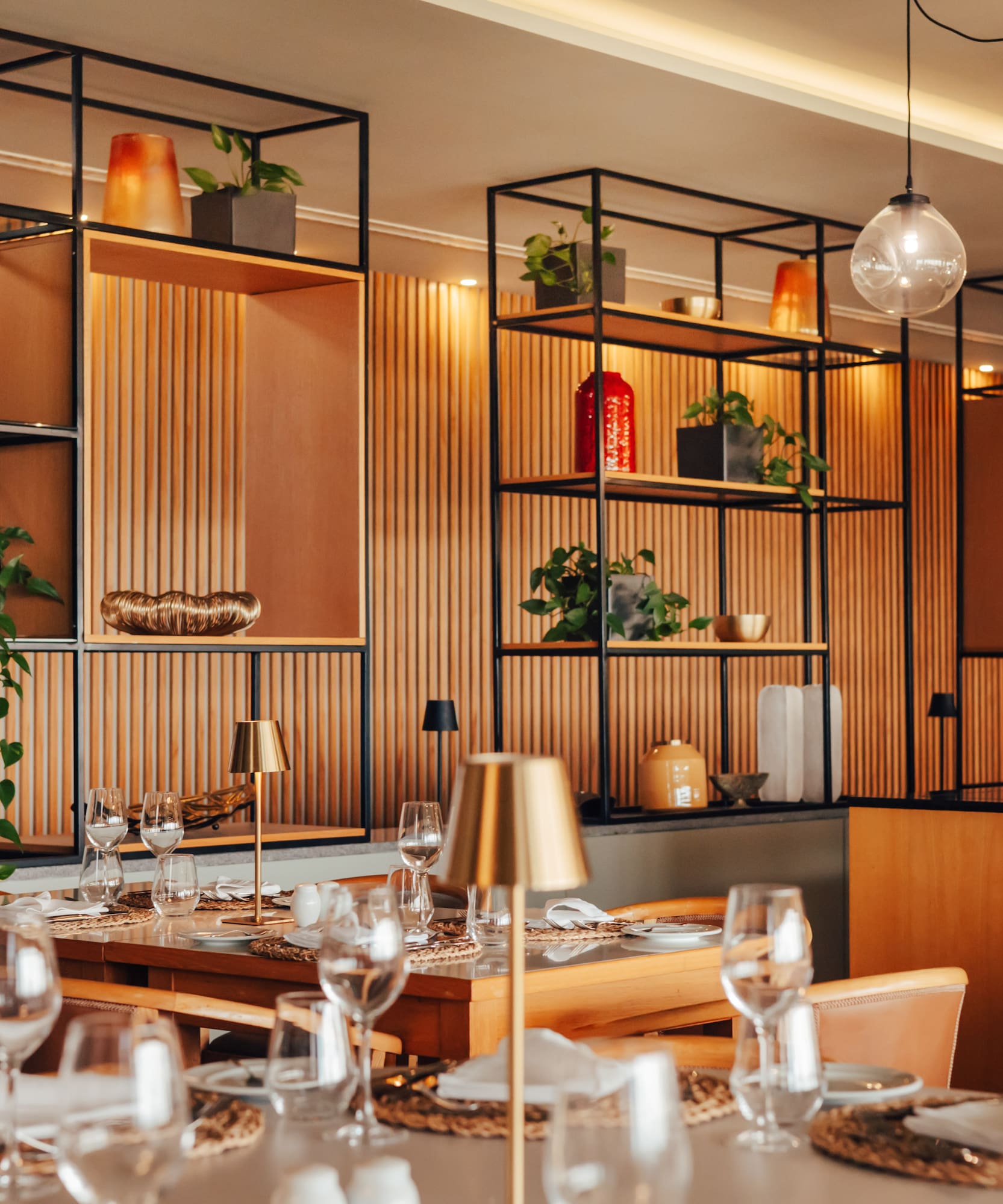 Elegant restaurant interior with modern decor, wooden shelves, and set tables.