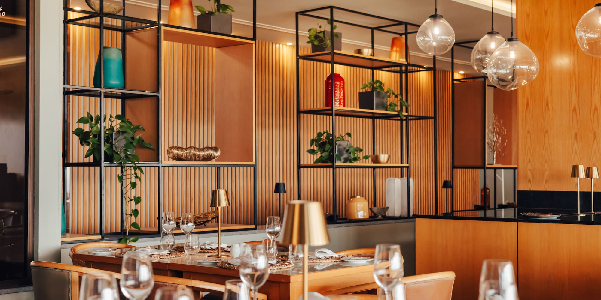 Modern restaurant dining room with set tables, decorative shelves, and warm lighting.