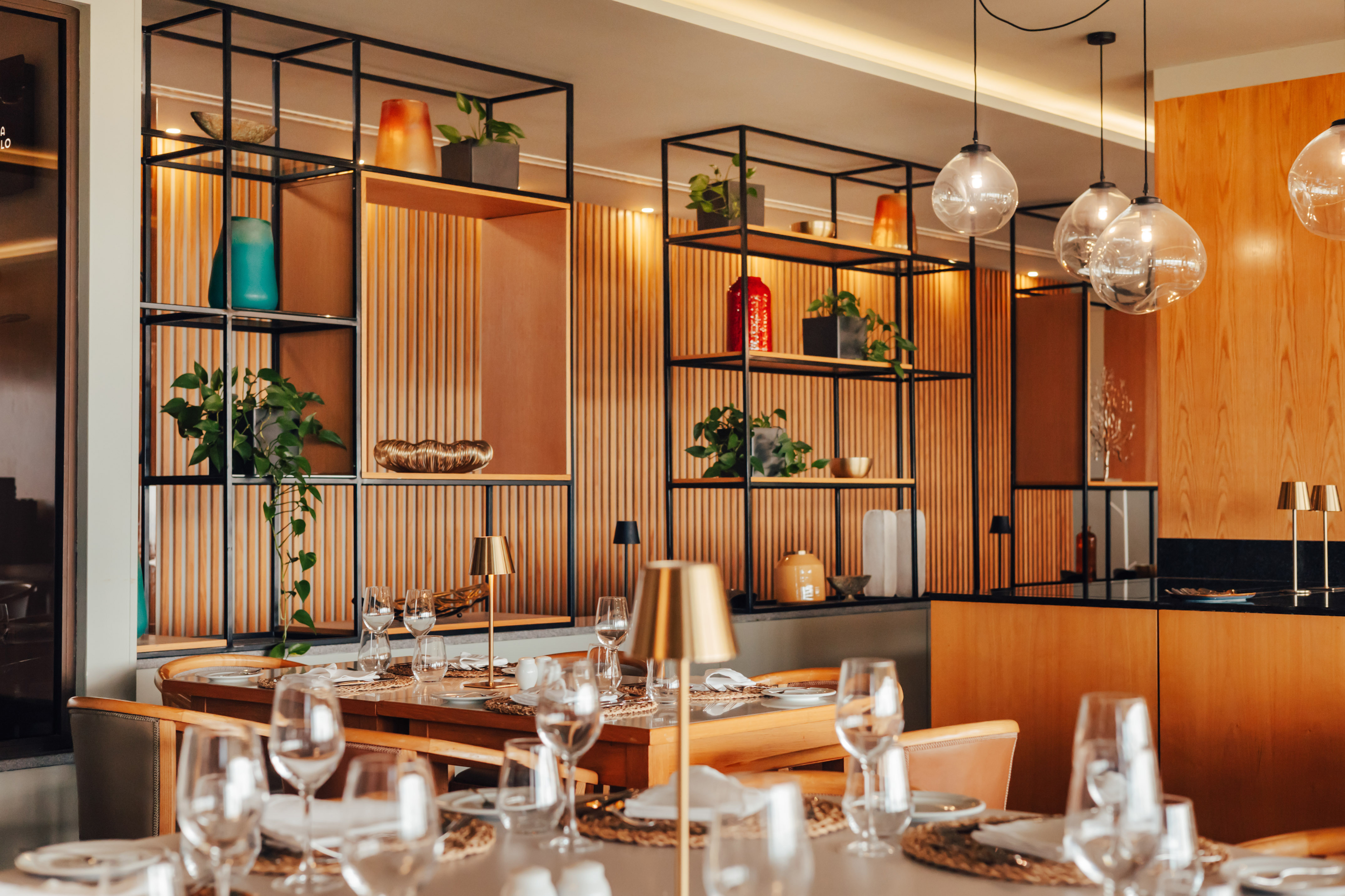 Elegant restaurant interior with modern decor, wooden shelves, and set tables.