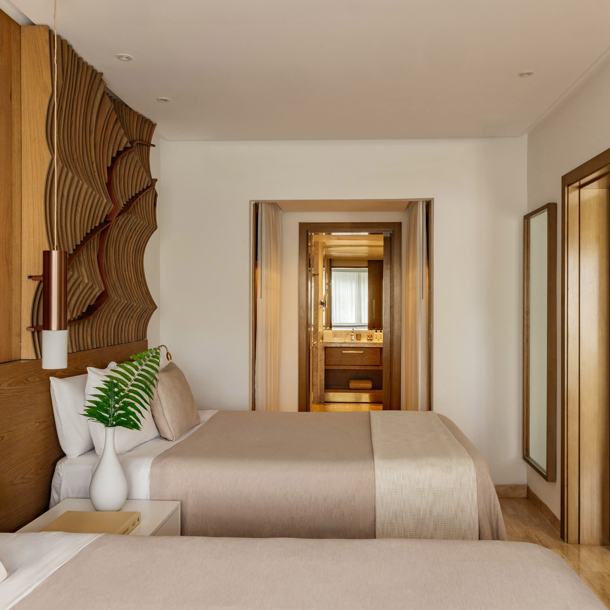Hotel bedroom with twin beds, natural wood headboard, and view into the bathroom.