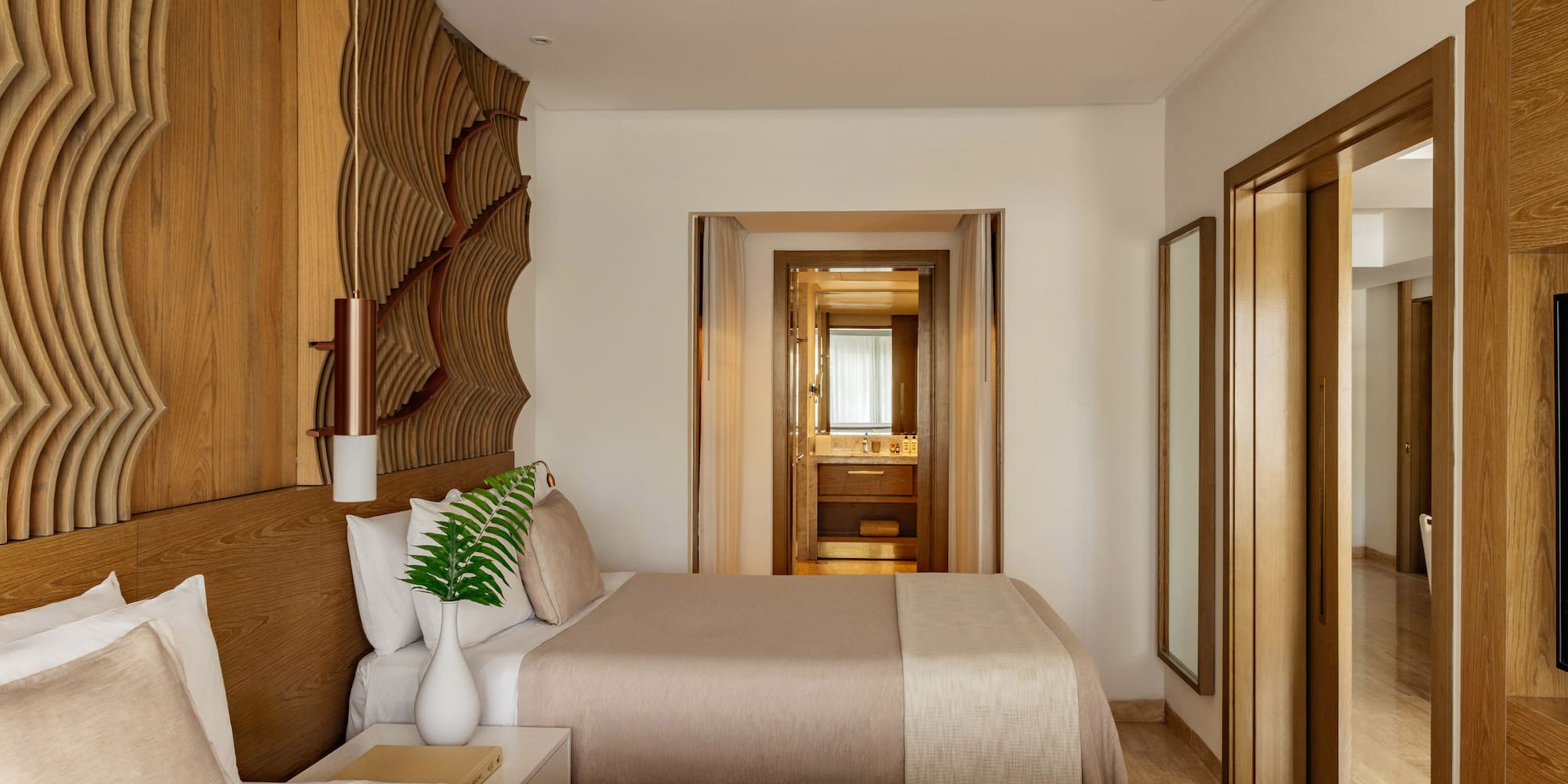 Hotel bedroom with twin beds, natural wood headboard, and view into the bathroom.
