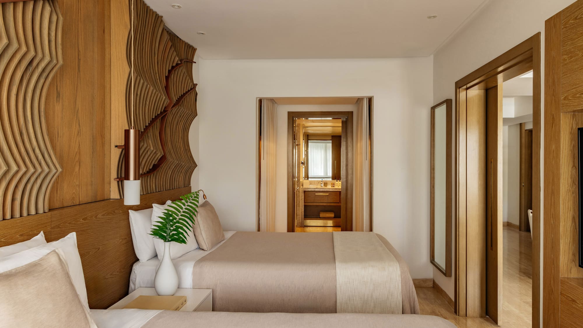 Hotel bedroom with twin beds, natural wood headboard, and view into the bathroom.