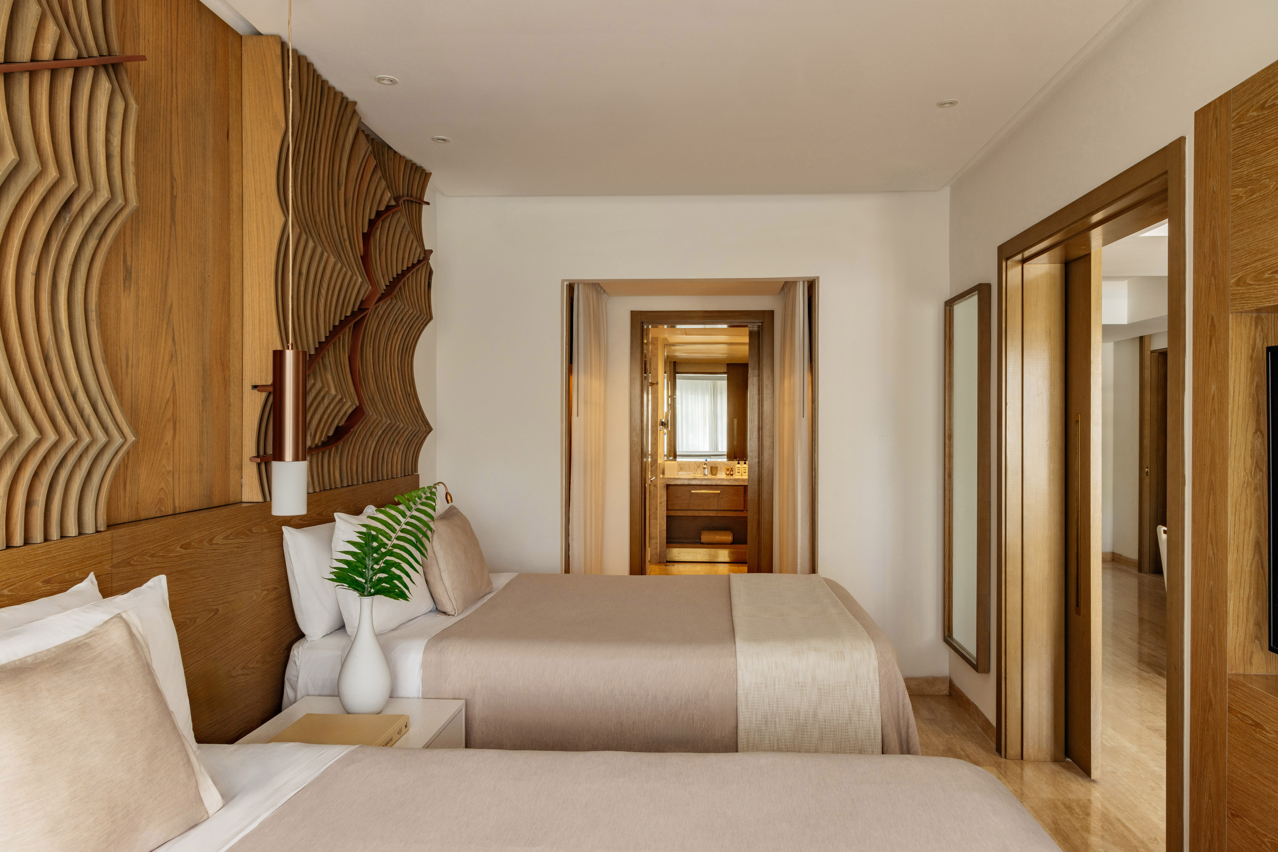 Hotel bedroom with twin beds, natural wood headboard, and view into the bathroom.