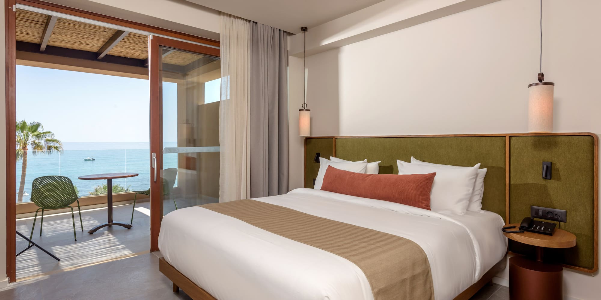 Modern hotel room with ocean view, private balcony, and king bed.