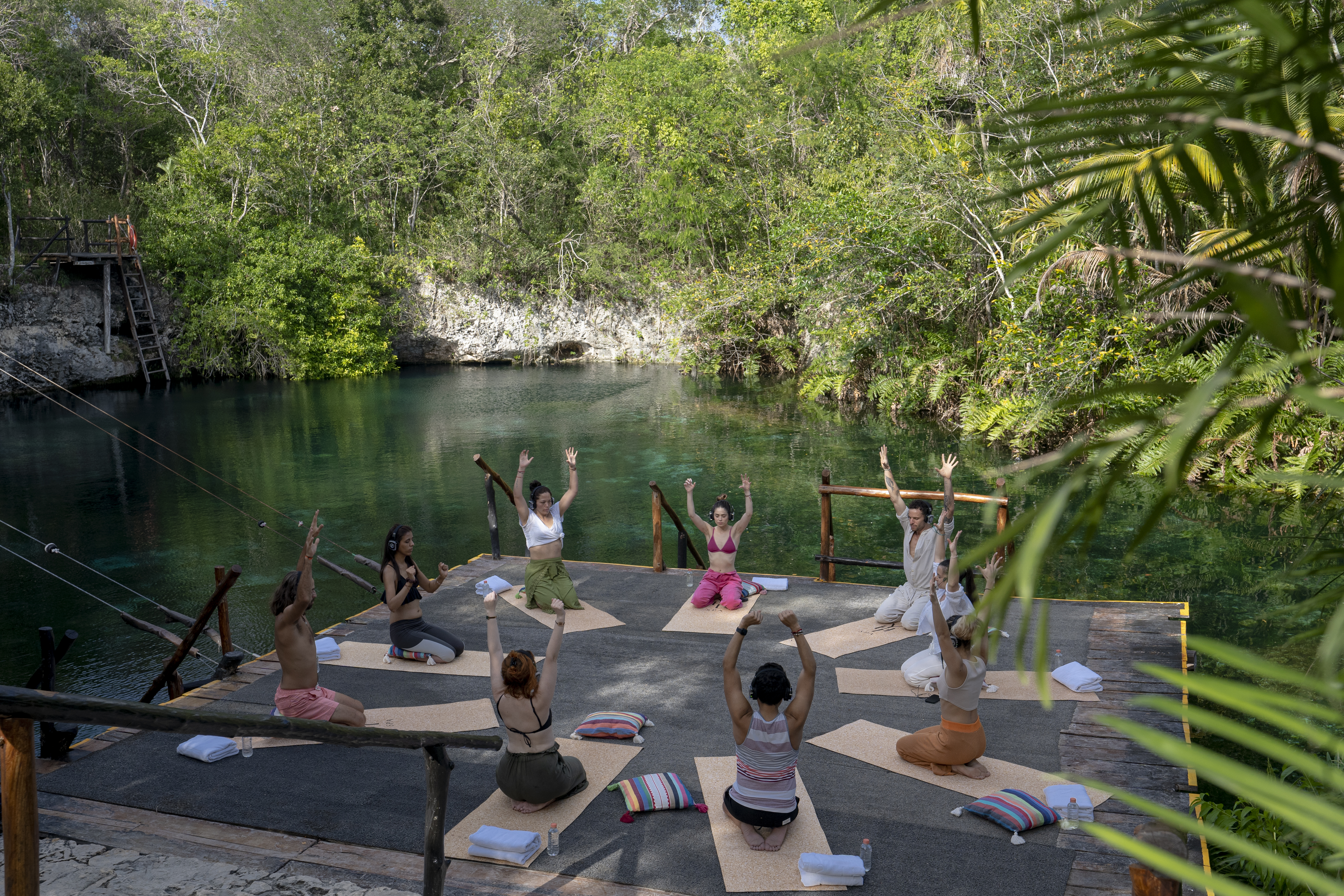 a group of people doing yoga outside by a body of water.