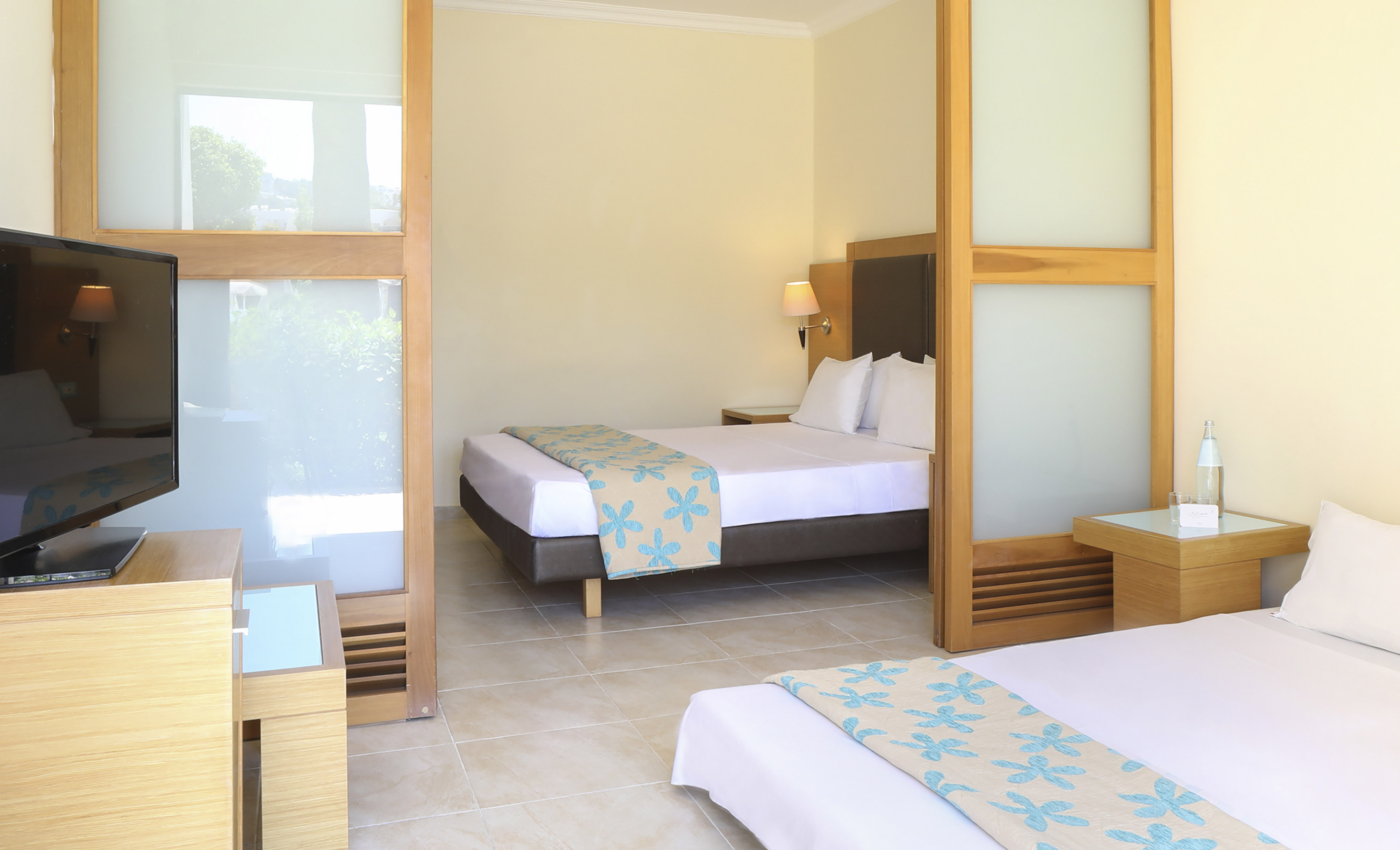 Hotel twin room with floral bedspreads, television, and frosted glass partition.