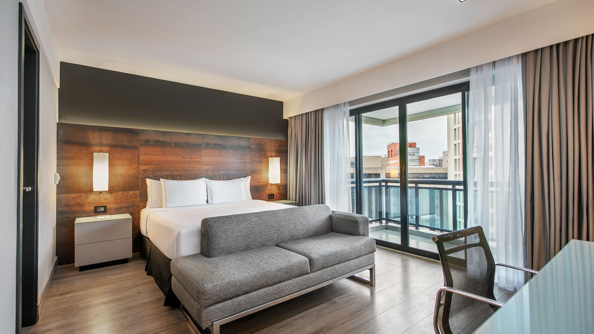 Quarto de hotel moderno com cama de casal, sofá cinza, escrivaninha e varanda. - Deluxe Queen Room com Varanda - Meliá Ibirapuera, São Paulo