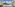 Hotel balcony overlooking turquoise sea, green trees, and distant coastal town.