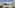 Hotel balcony overlooking turquoise sea, green trees, and distant coastal town.
