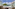 Hotel balcony overlooking turquoise sea, green trees, and distant coastal town.