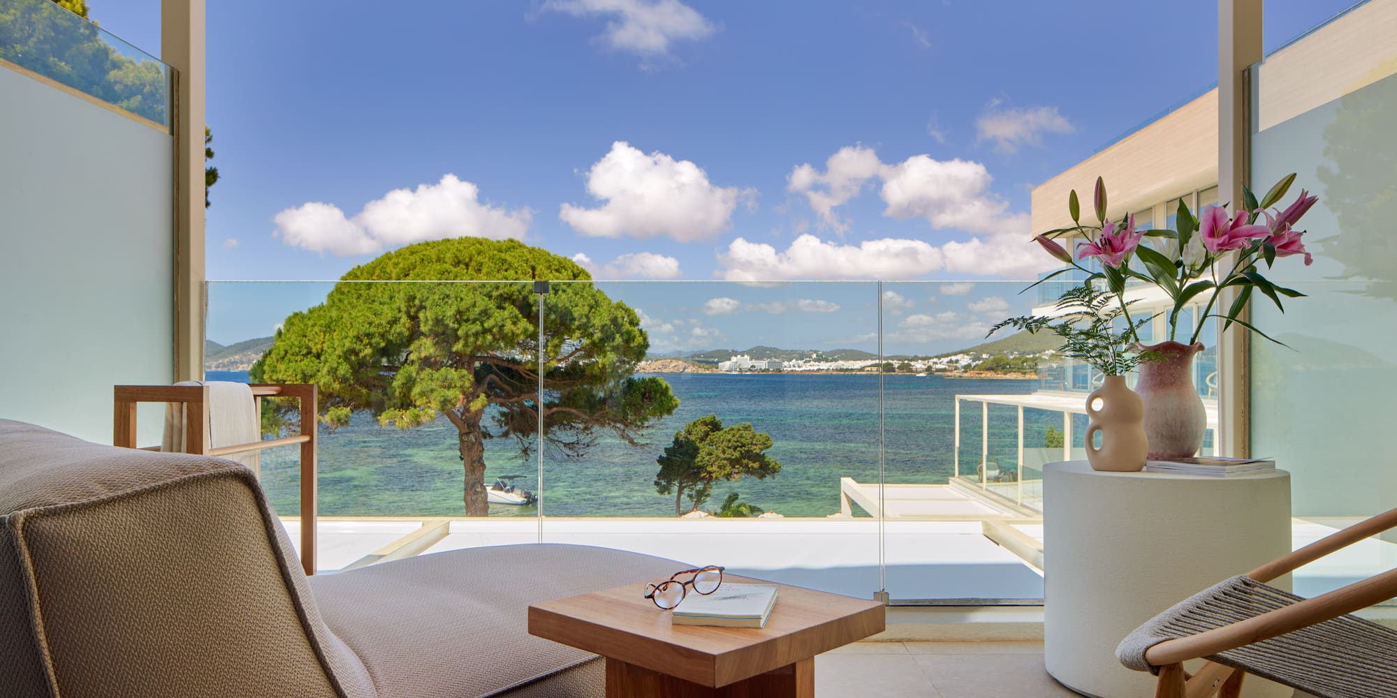 Hotel balcony overlooking turquoise sea, green trees, and distant coastal town.