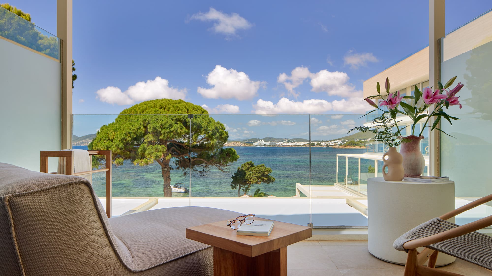 Hotel balcony overlooking turquoise sea, green trees, and distant coastal town.