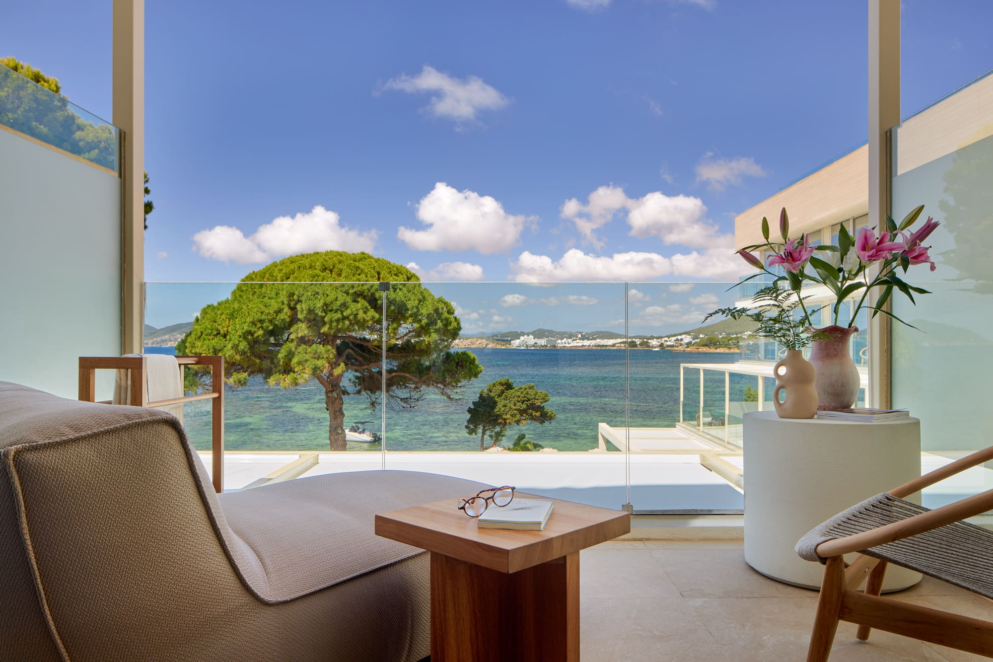 Hotel balcony overlooking turquoise sea, green trees, and distant coastal town.