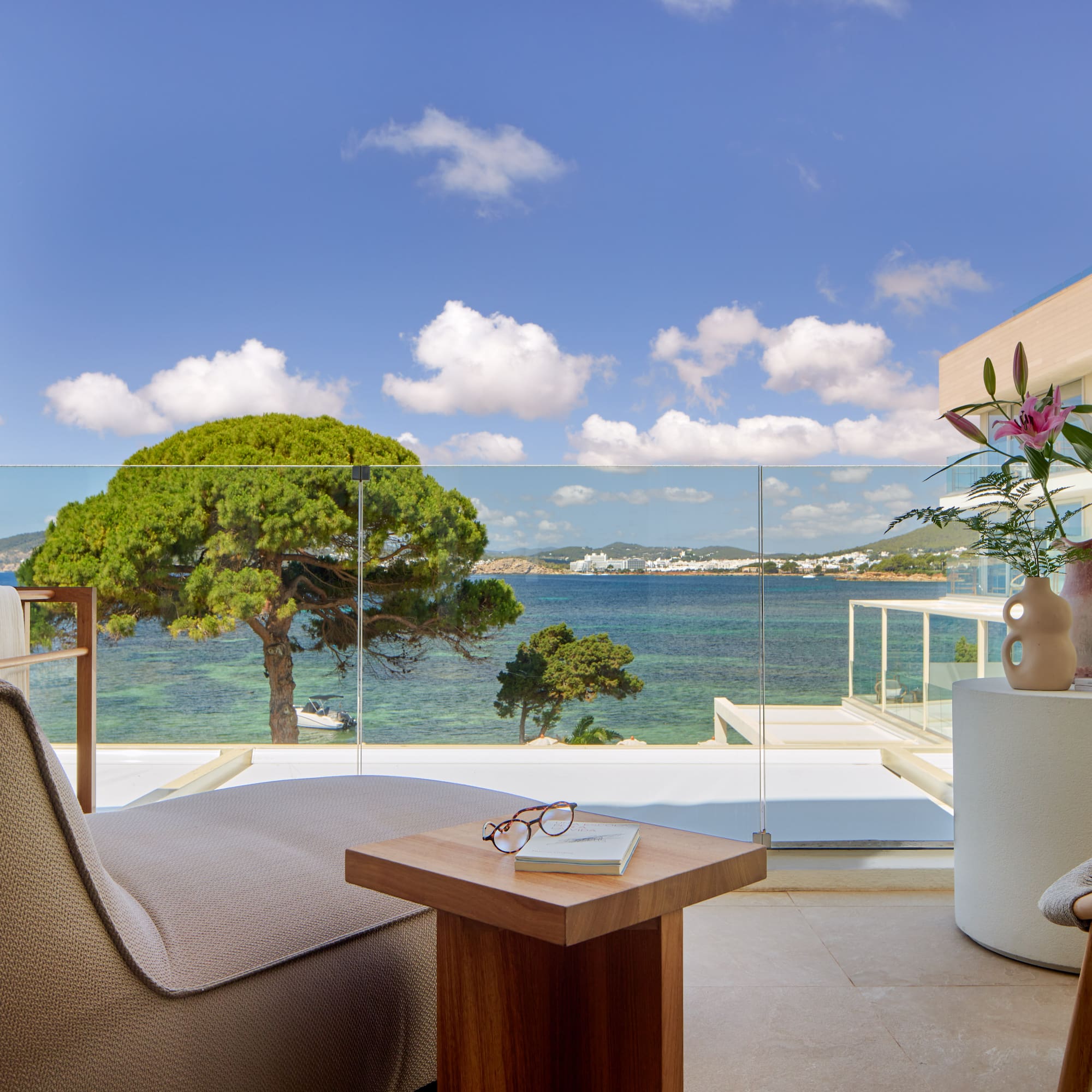 Hotel balcony overlooking turquoise sea, green trees, and distant coastal town.