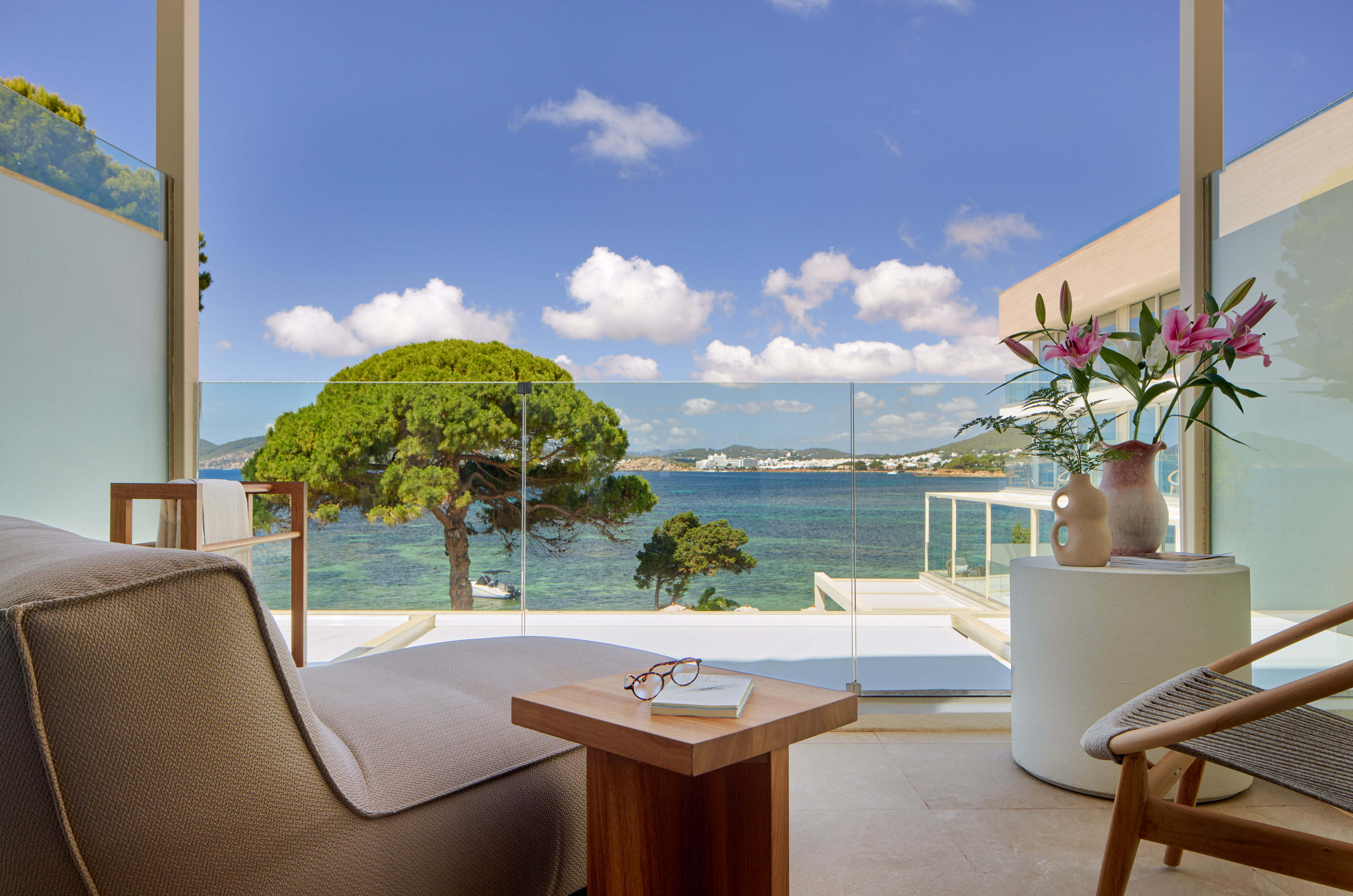 Hotel balcony overlooking turquoise sea, green trees, and distant coastal town.
