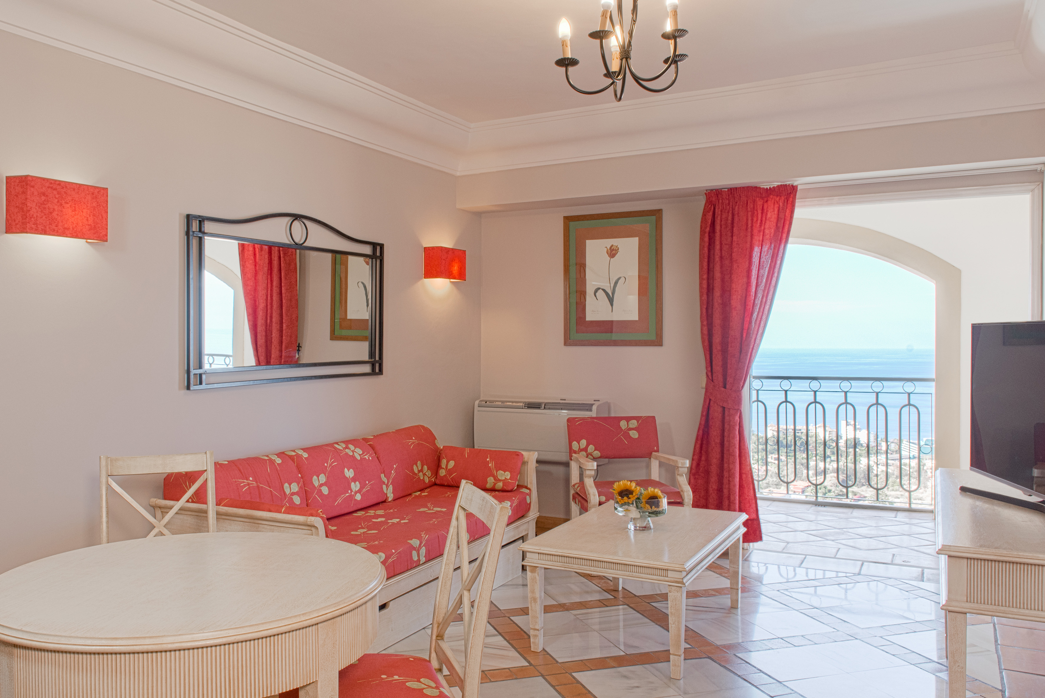 Hotel living room suite with red sofa, dining area, and ocean view balcony.