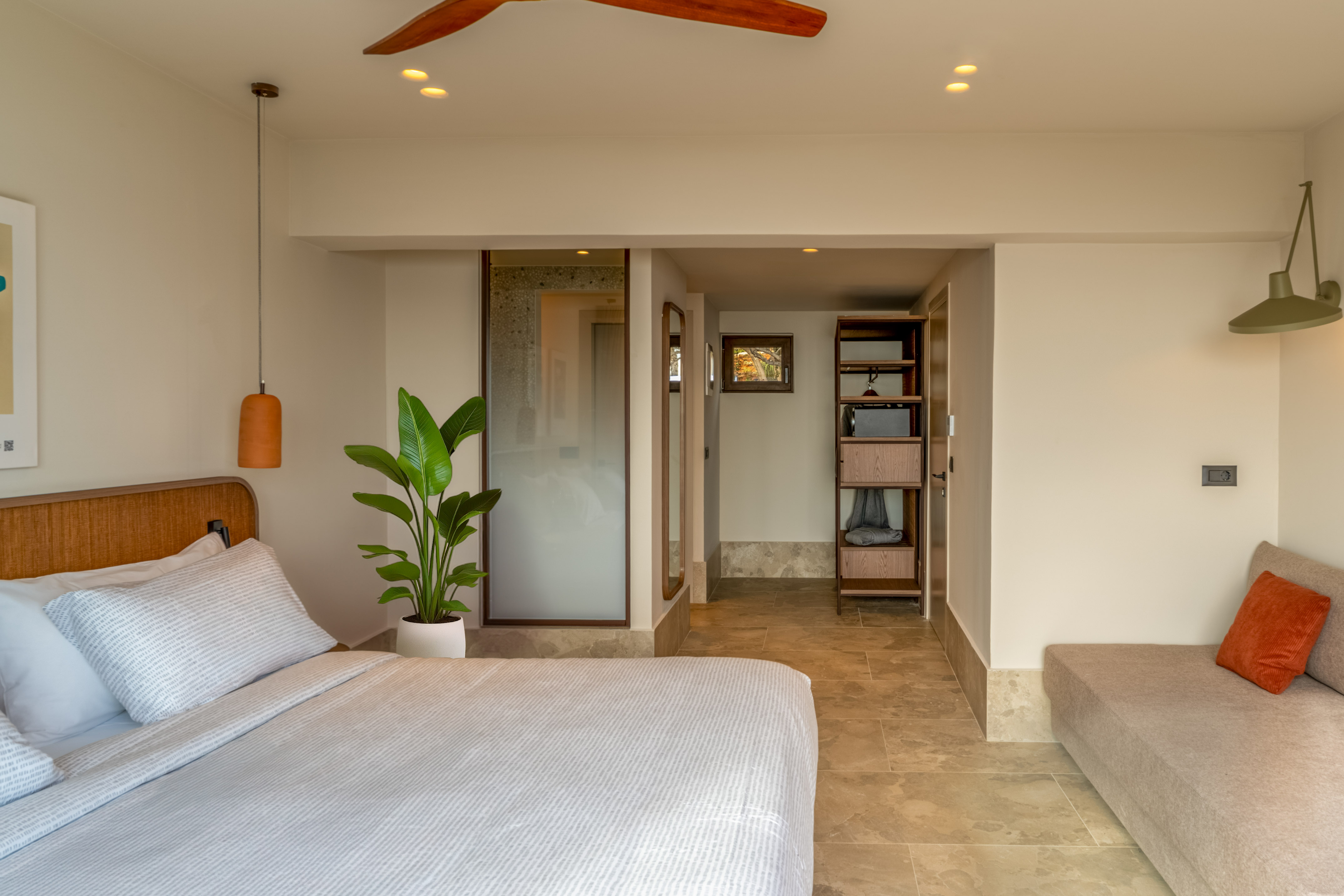 Modern bedroom with white bed, green plant, wood shelving, and tiled floor.