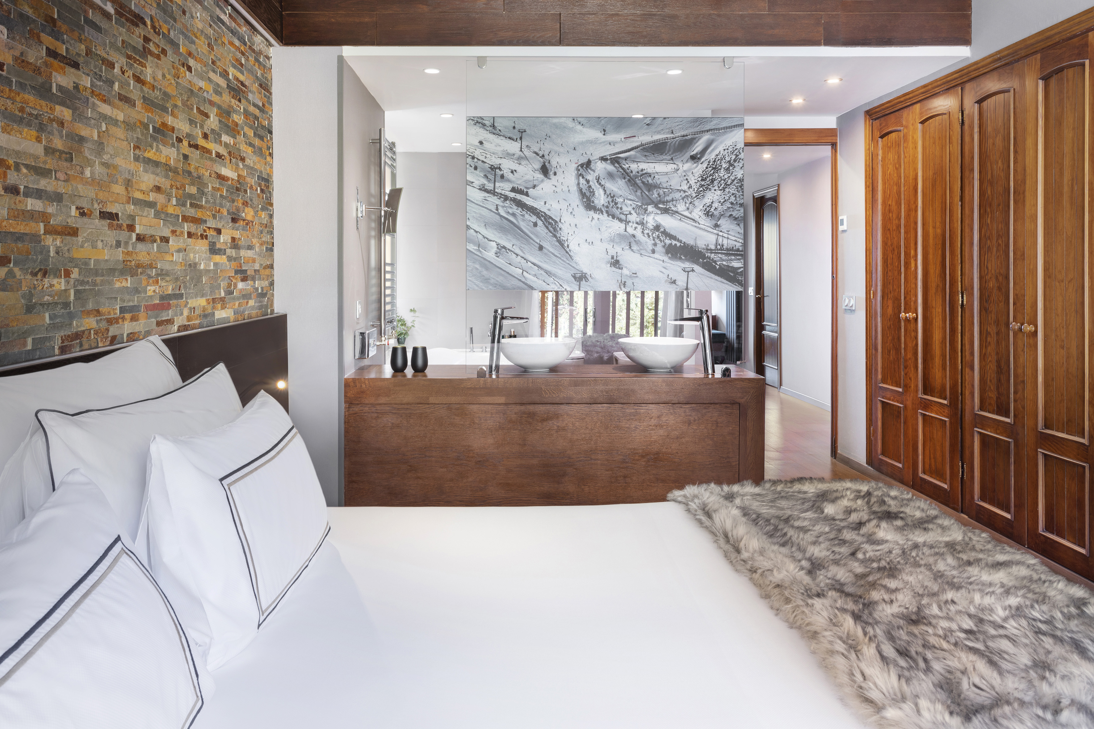 Modern bedroom featuring stone wall, ski art, open bath, double vanity.