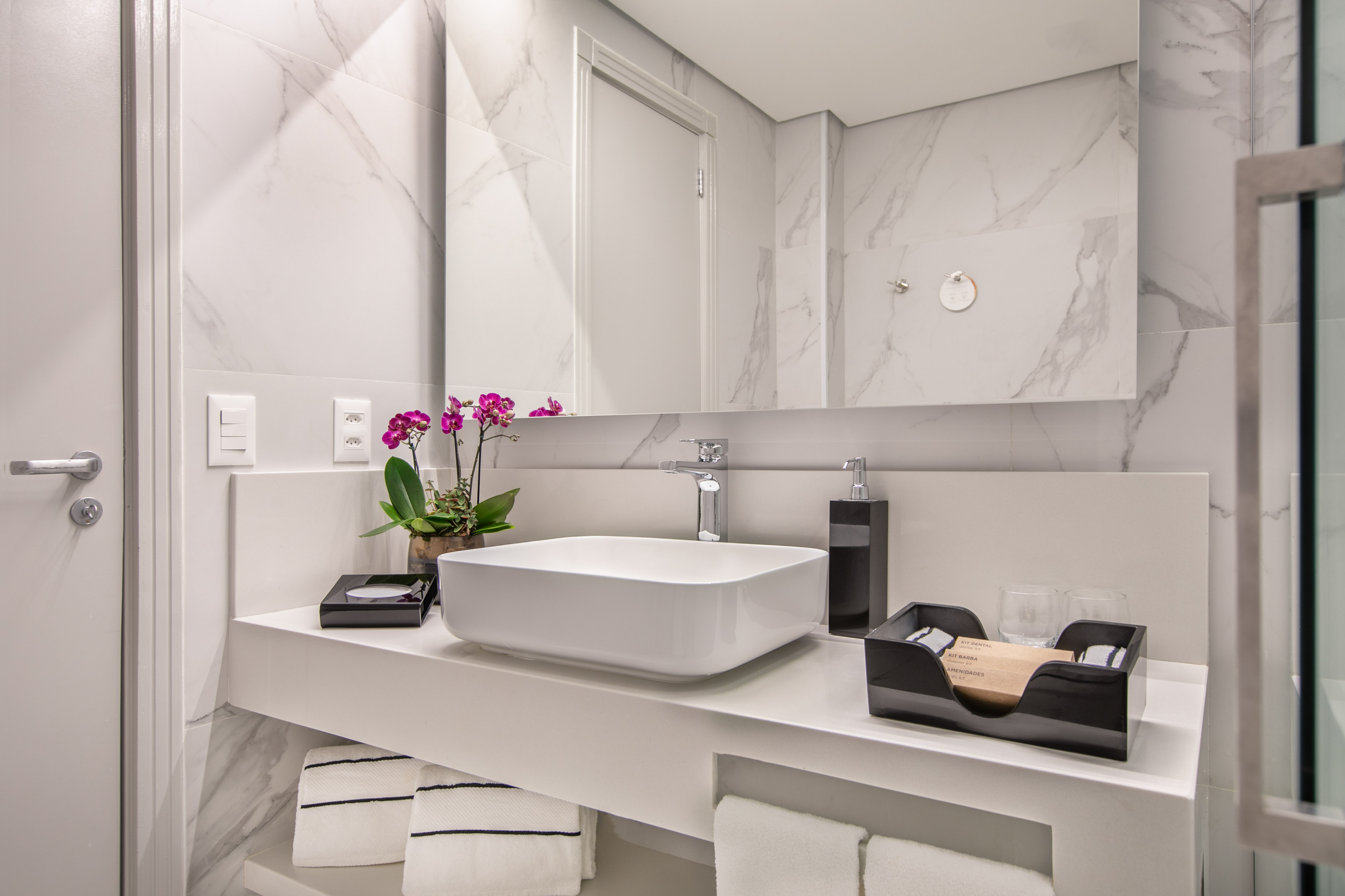White marble modern bathroom vanity with rectangular sink, amenities, and orchid.