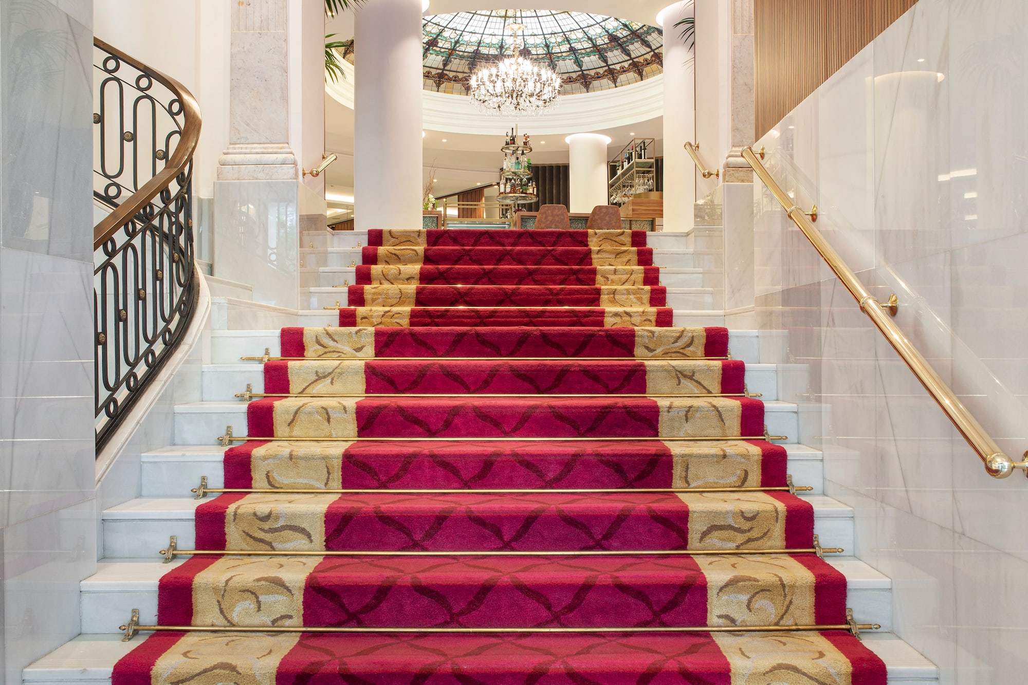 Grand marble staircase with red and gold patterned runner carpet in a luxury hotel lobby.