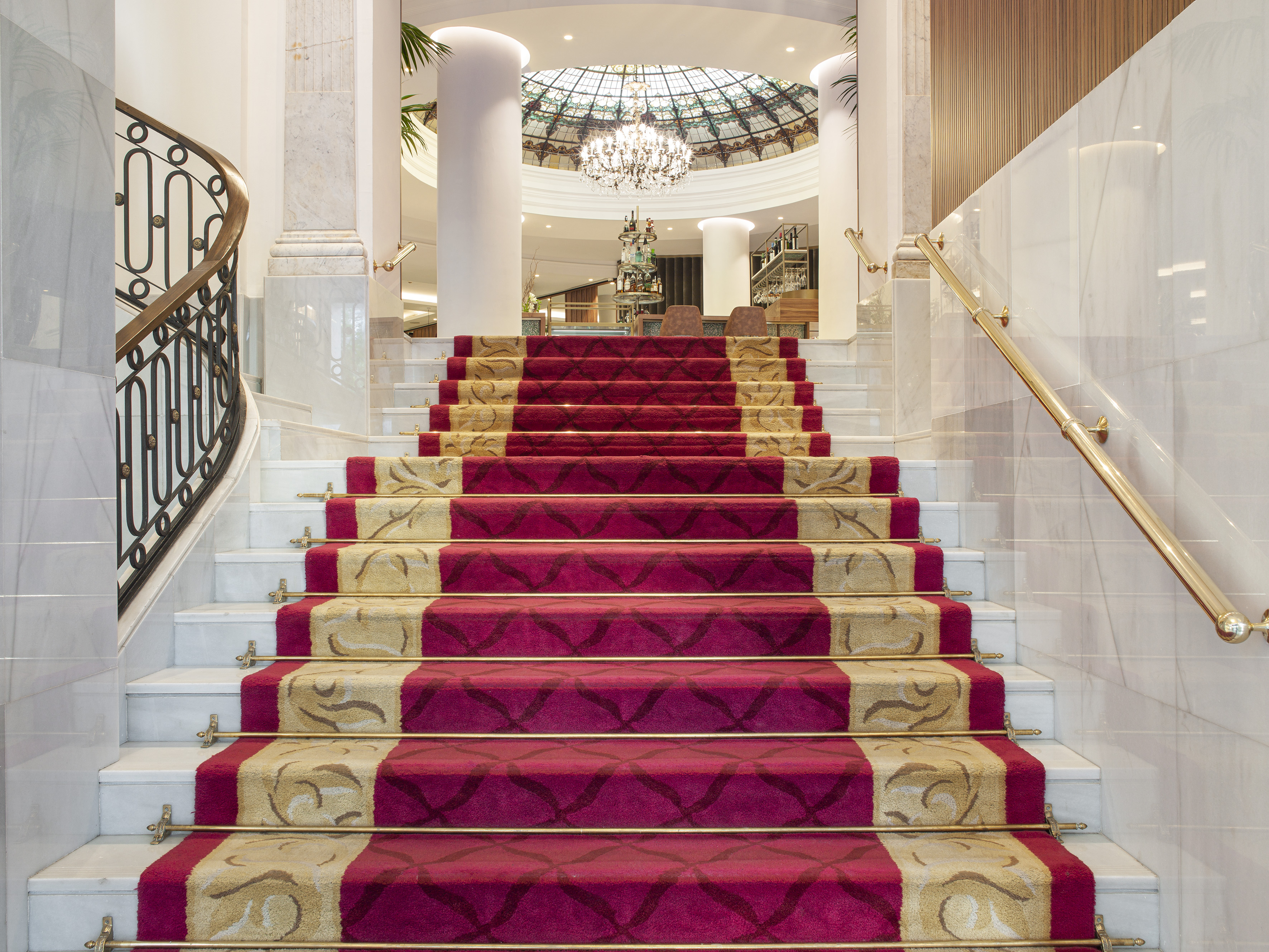 Grand marble staircase with red and gold patterned runner carpet in a luxury hotel lobby.
