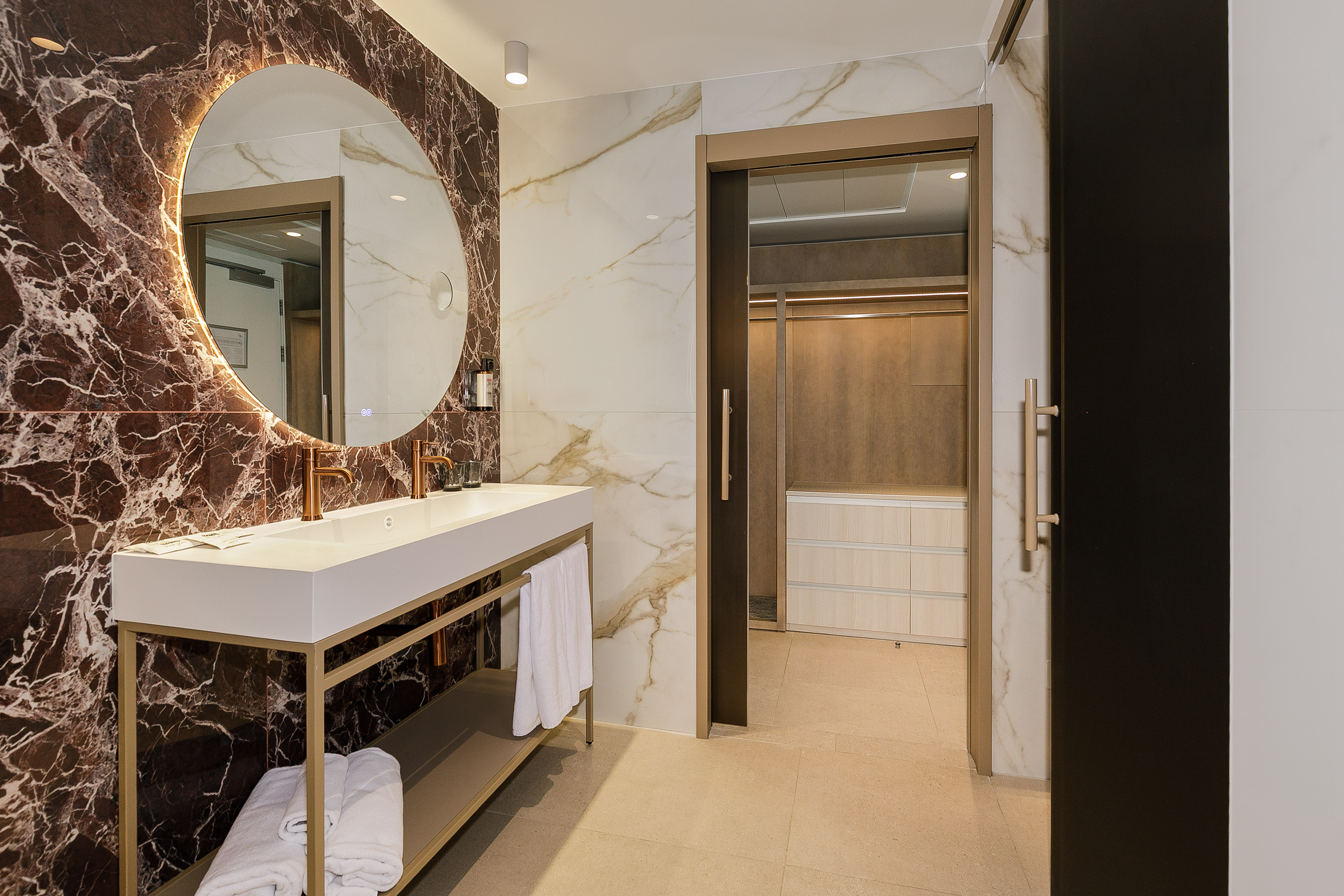 Modern marble bathroom with backlit mirror, double vanity, and walk-in closet.