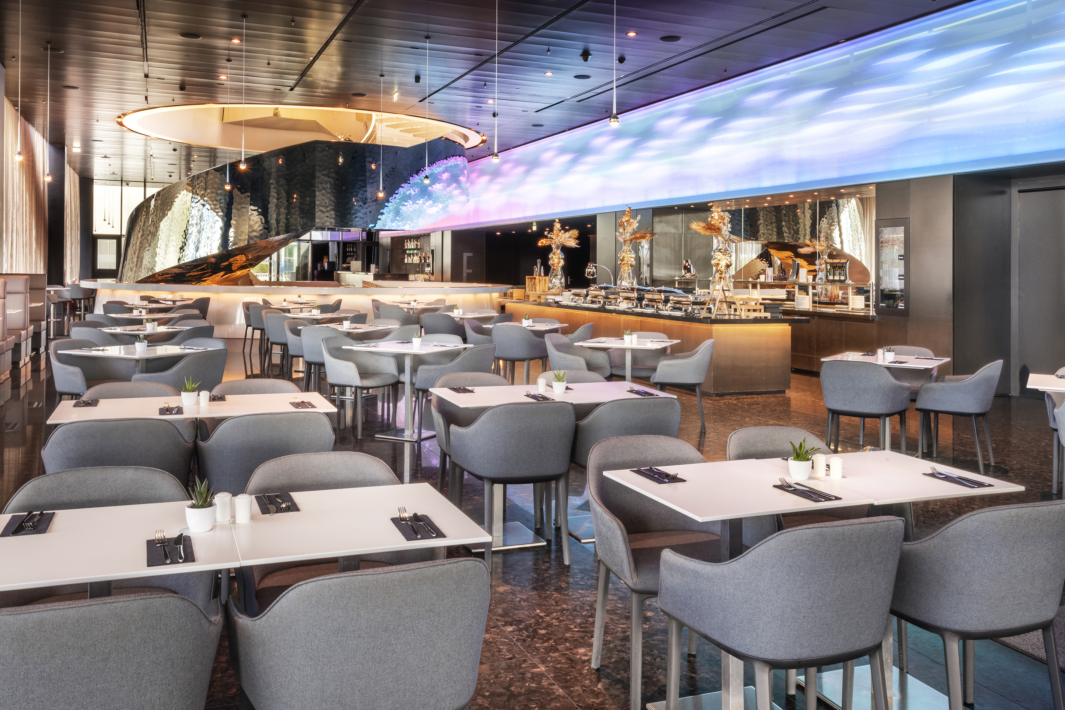 Modern restaurant dining area with buffet, grey chairs, and illuminated bar.