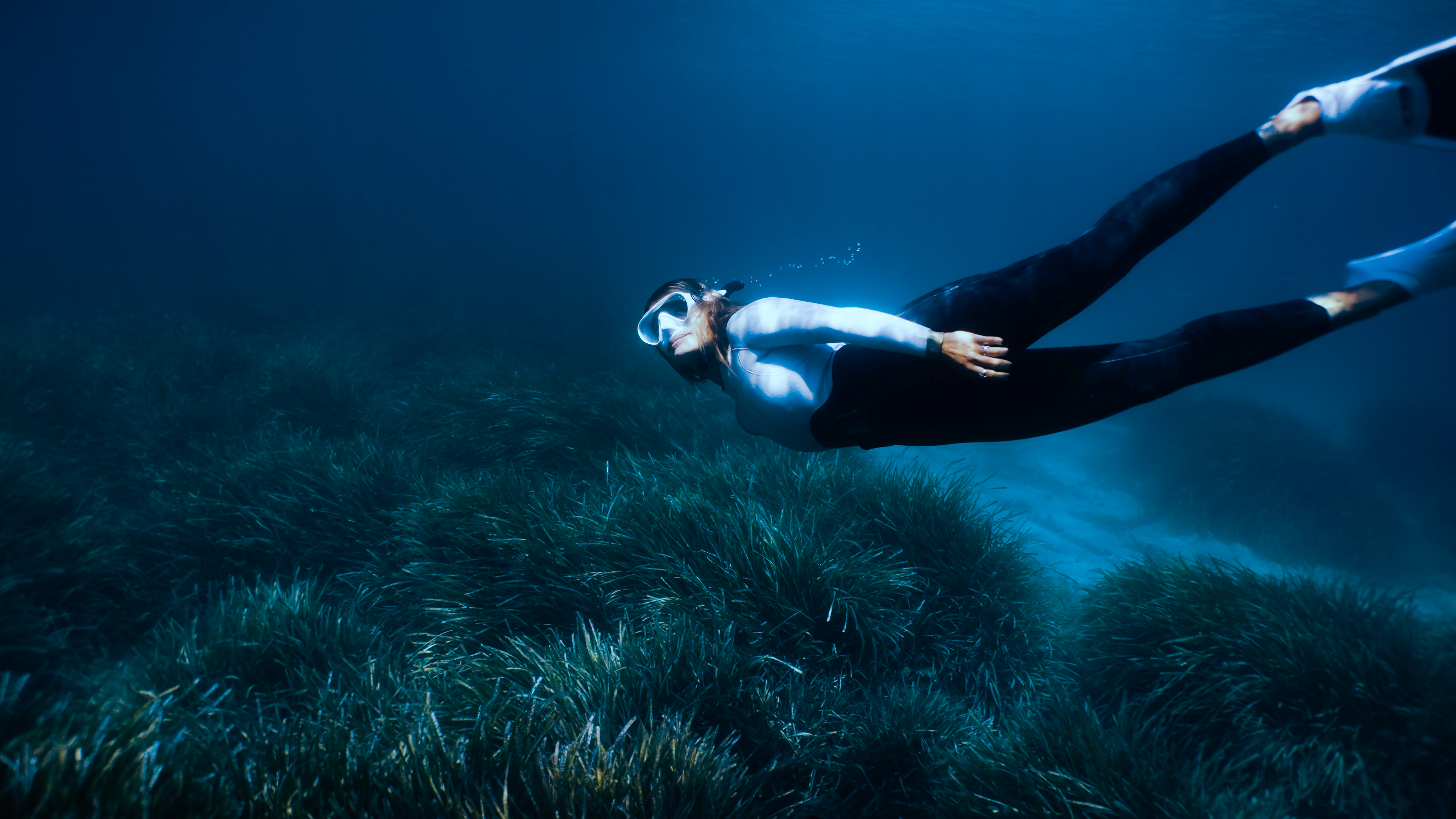 Freediver in wetsuit and mask swimming over lush seagrass.