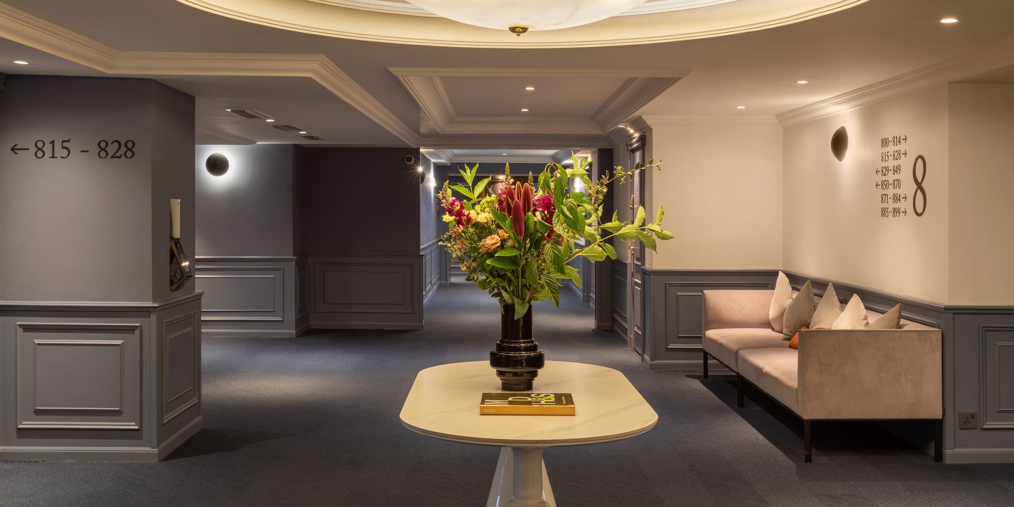 Elegant hotel corridor with floral arrangement, sofa, and room number signs.