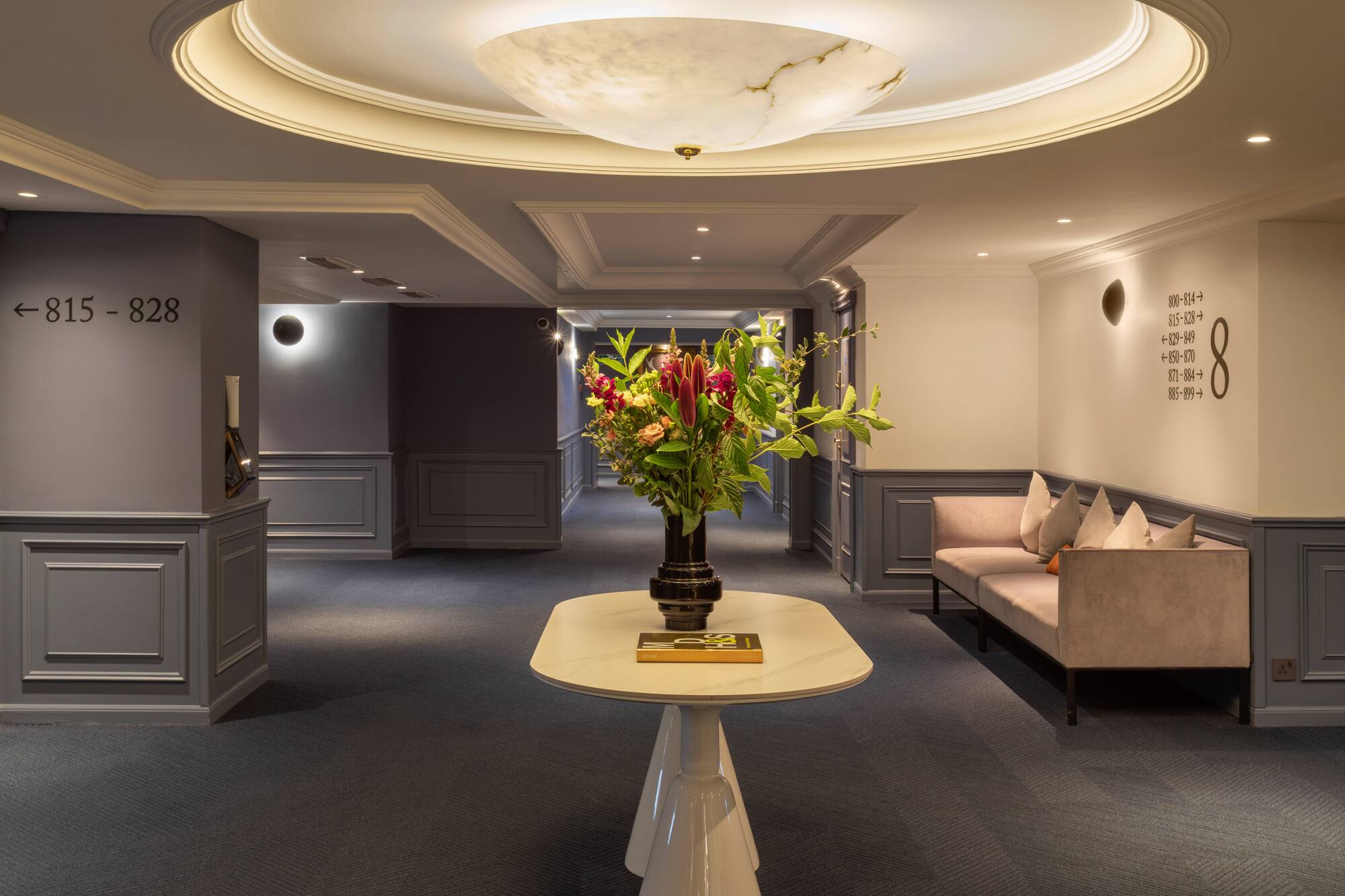 Elegant hotel corridor with floral arrangement, sofa, and room number signs.