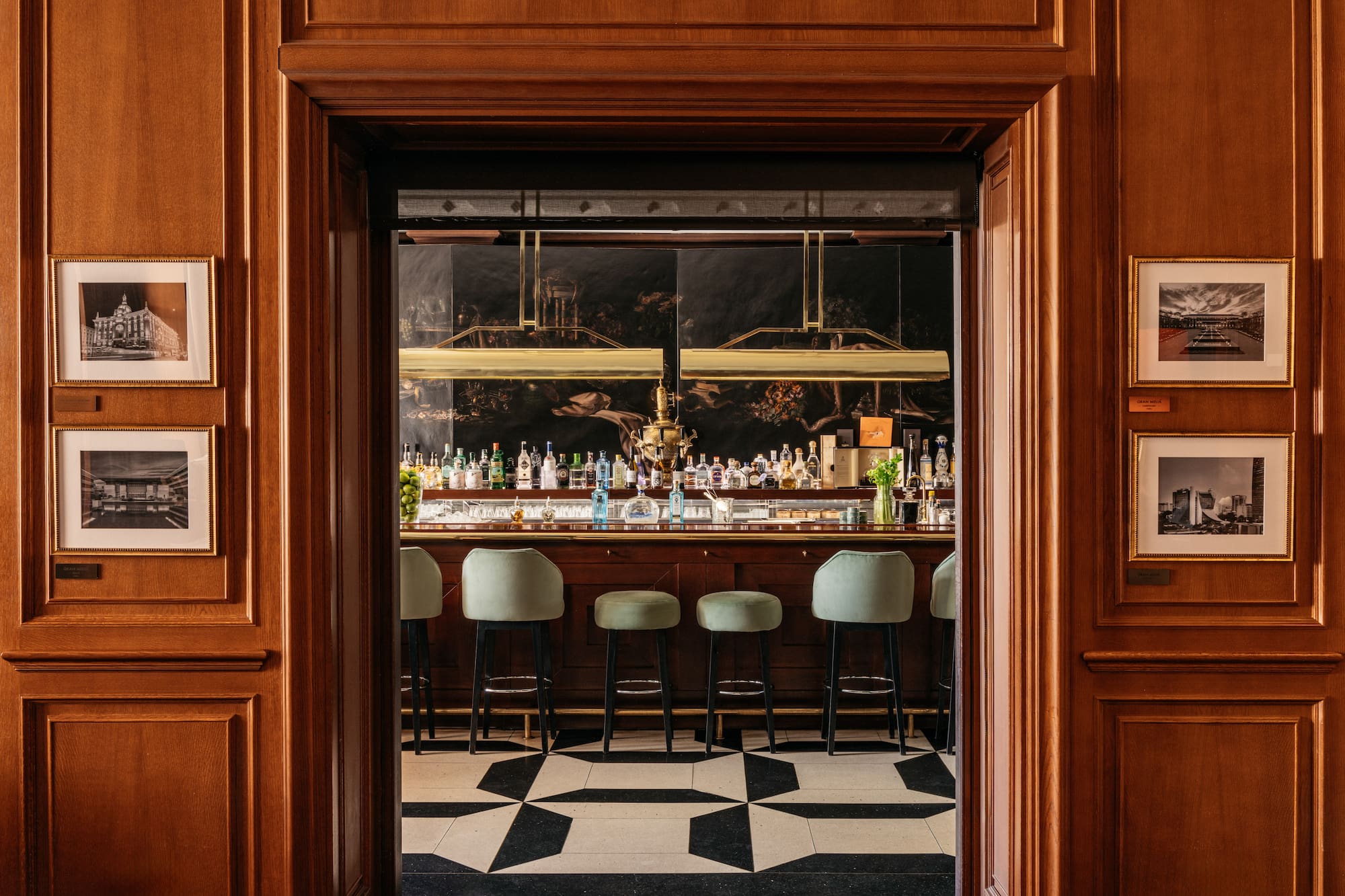 Elegant hotel bar viewed through a carved wooden entryway, green stools.