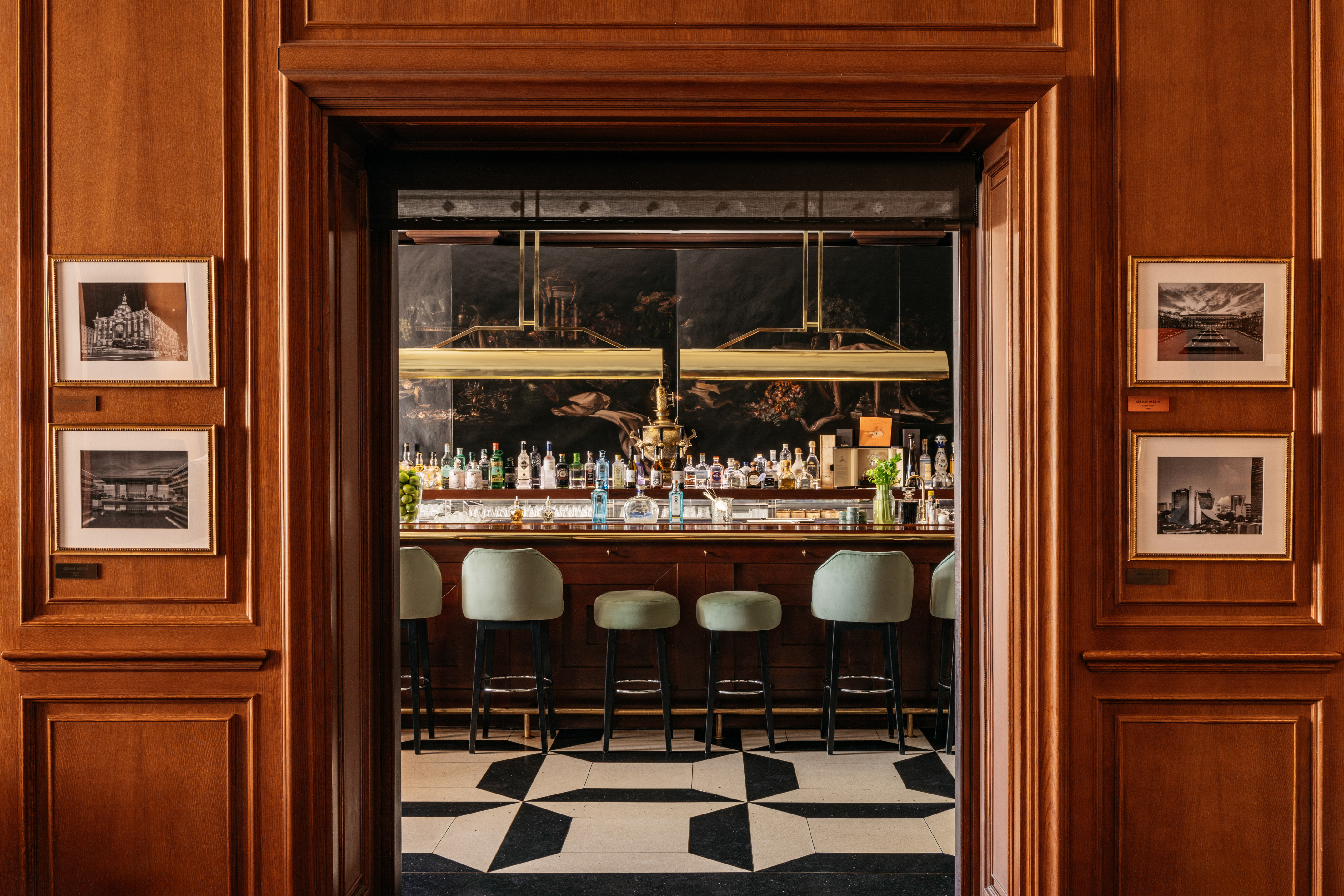 Elegant hotel bar viewed through a carved wooden entryway, green stools.