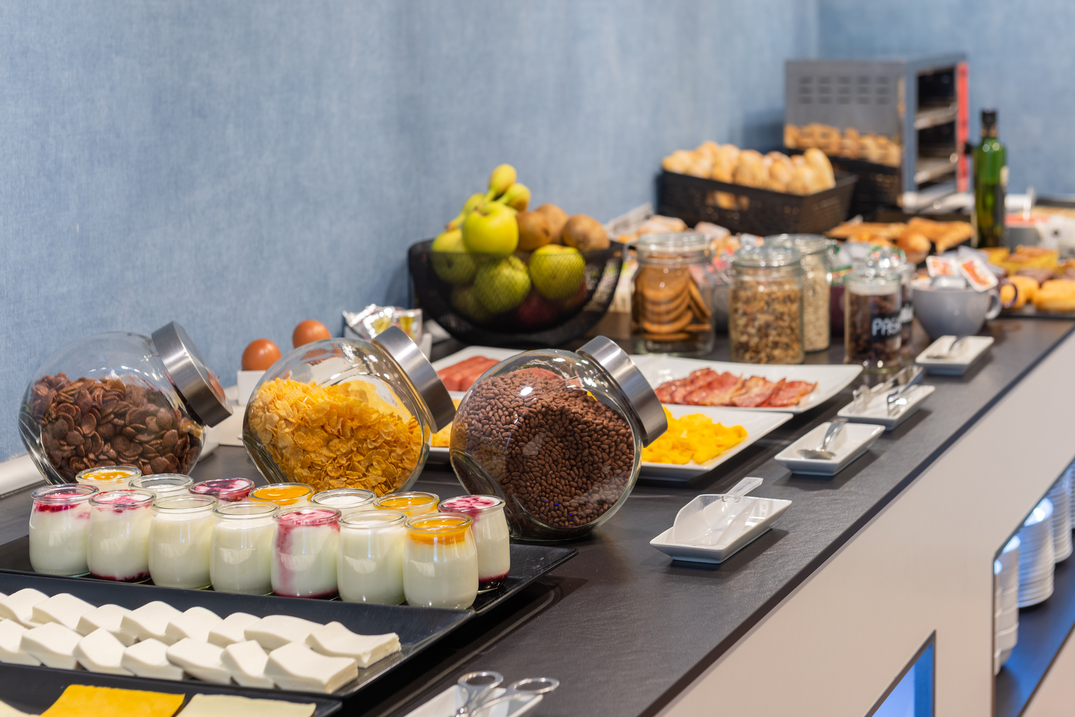 Breakfast buffet featuring yogurts, cereals, fresh fruit, and baked goods.