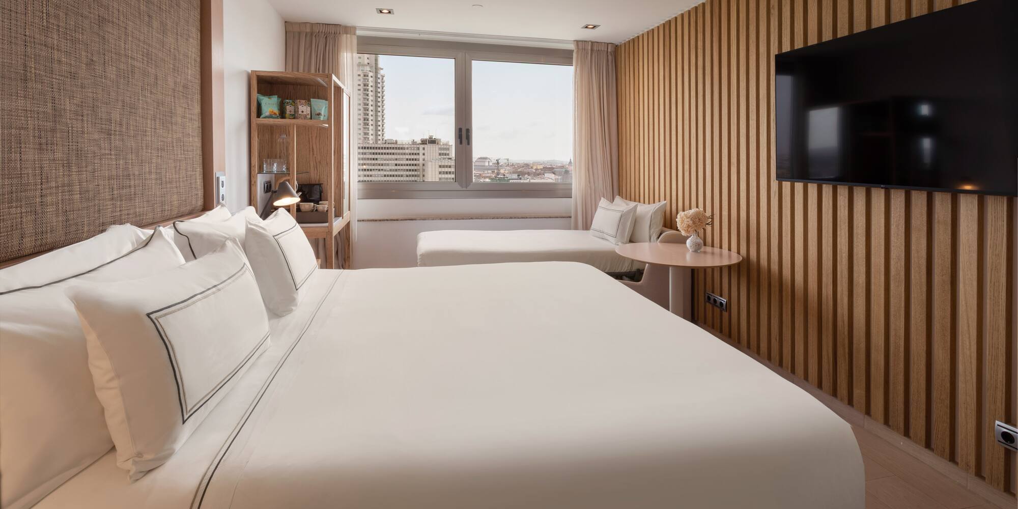 Modern hotel room with king bed, wood slatted wall, and city window view.