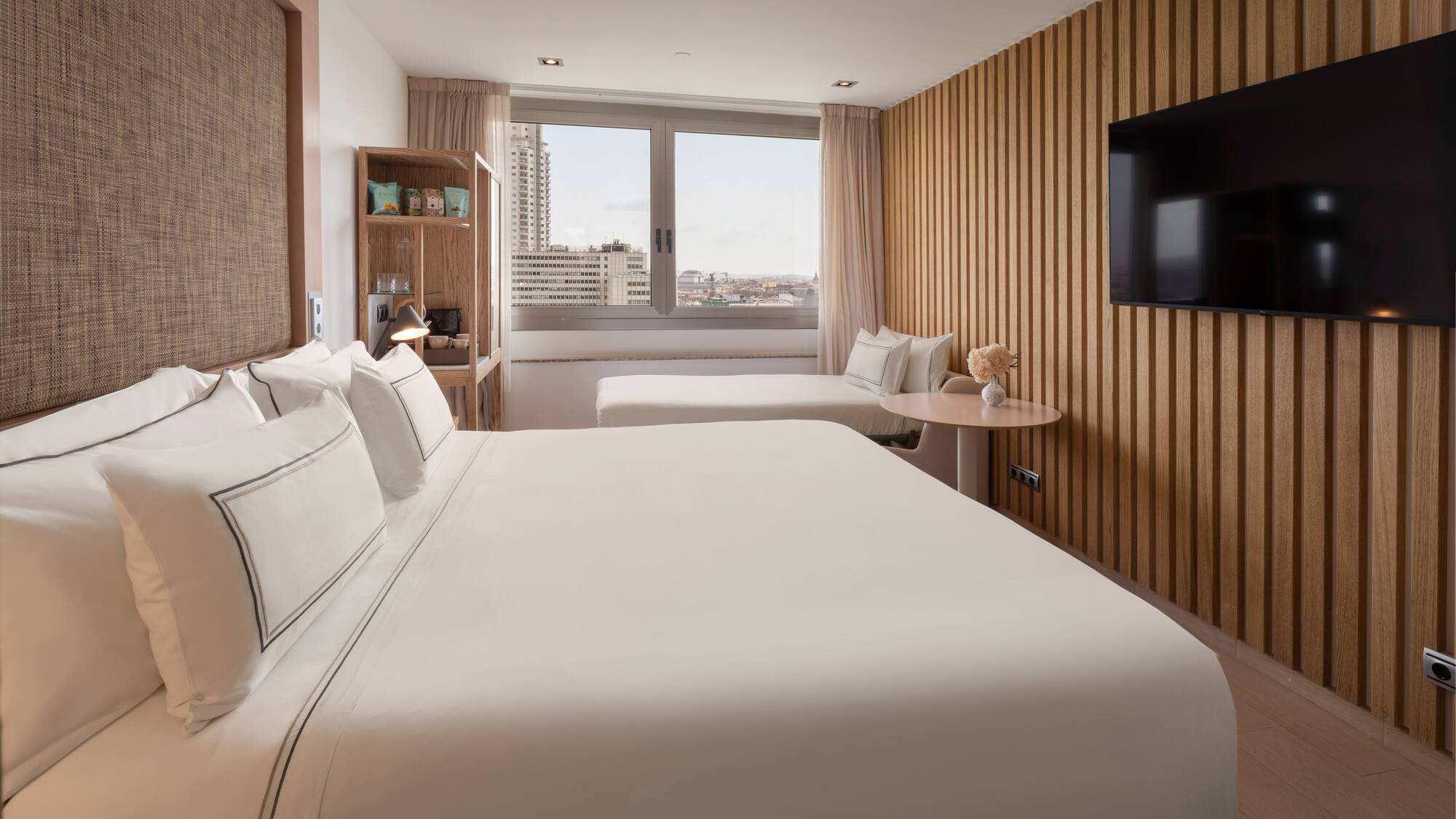 Modern hotel room with king bed, wood slatted wall, and city window view.