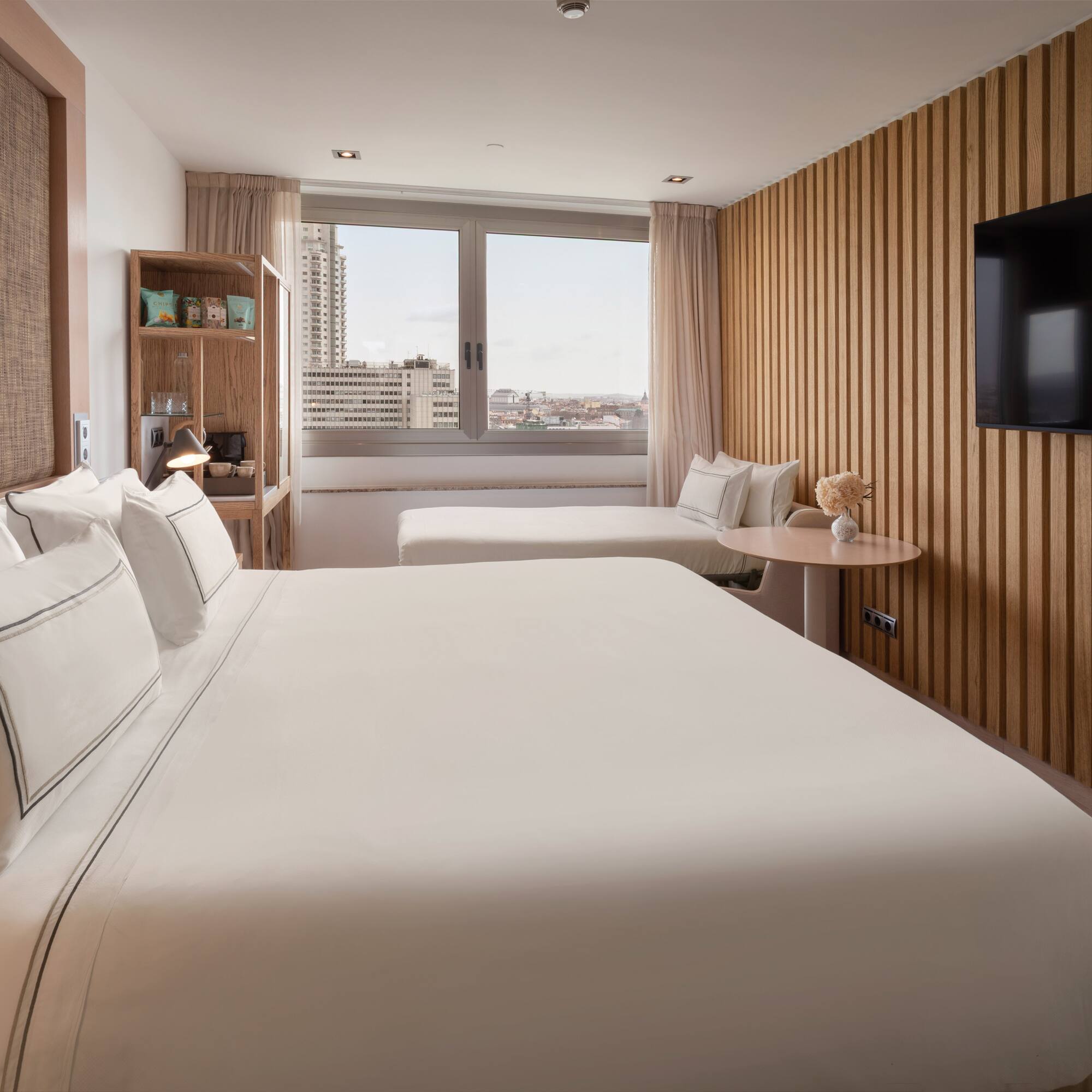 Modern hotel room with king bed, wood slatted wall, and city window view.