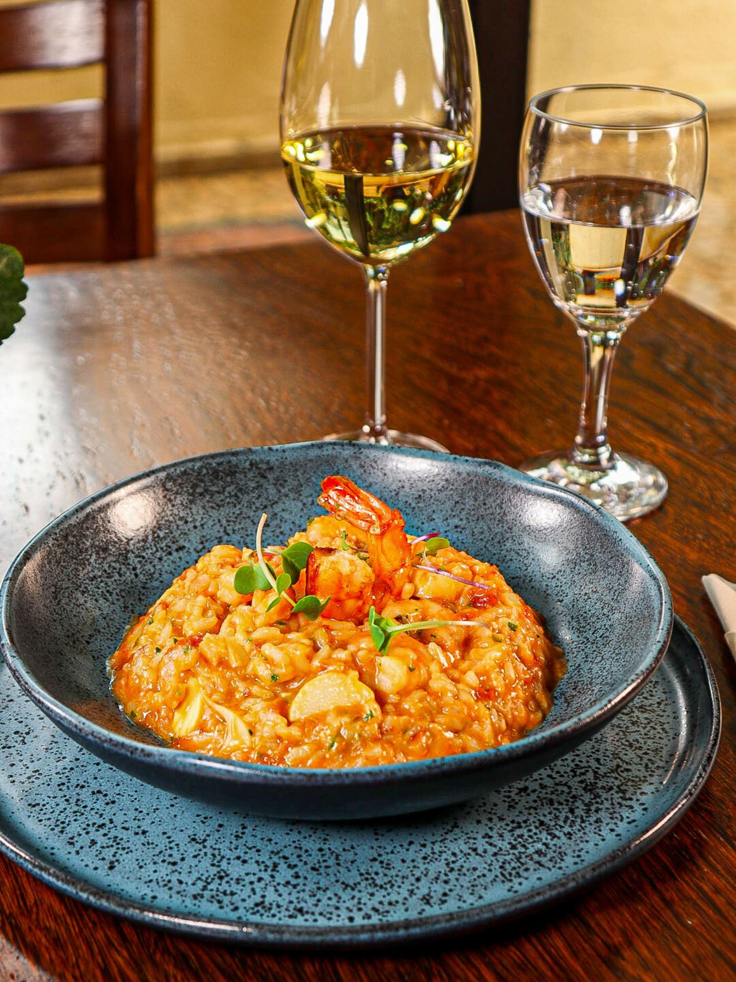 a bowl of food on a plate next to wine glasses
