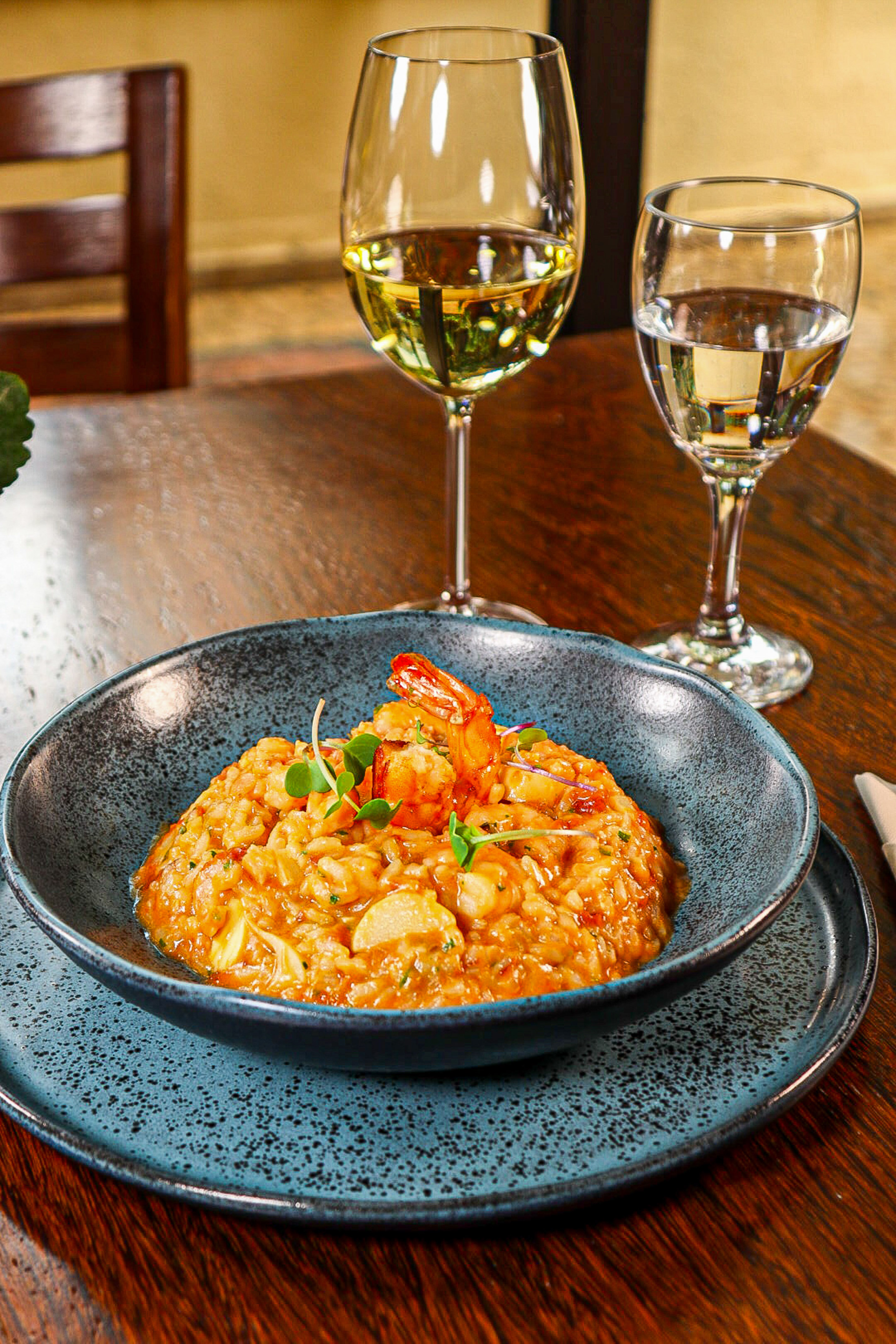 Shrimp risotto garnished with microgreens, white wine on a wooden table.