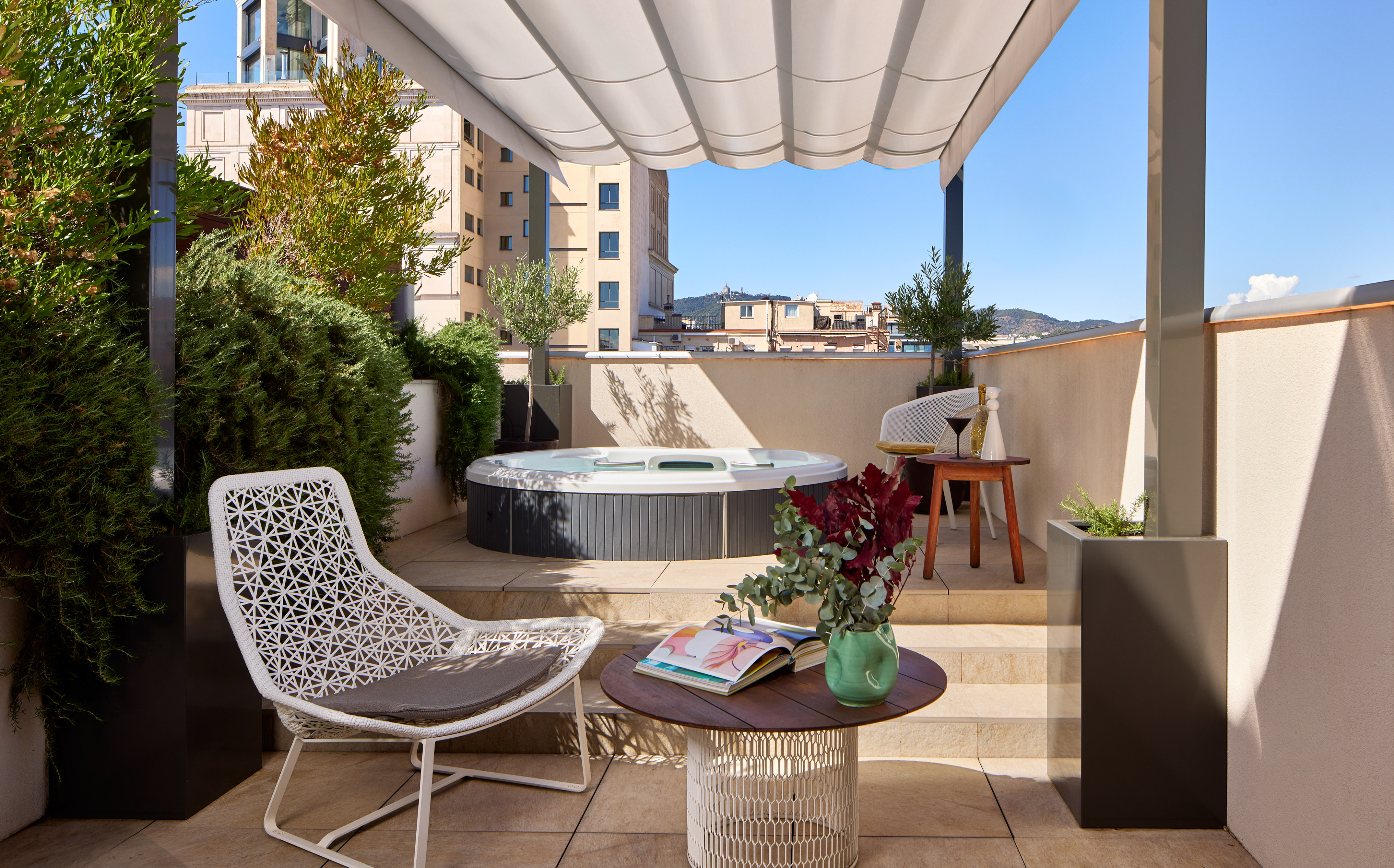 Rooftop terrace with hot tub, lounge chairs, lush plants, and city view.