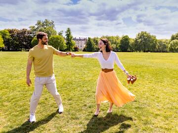 a man and woman holding hands and walking in a park