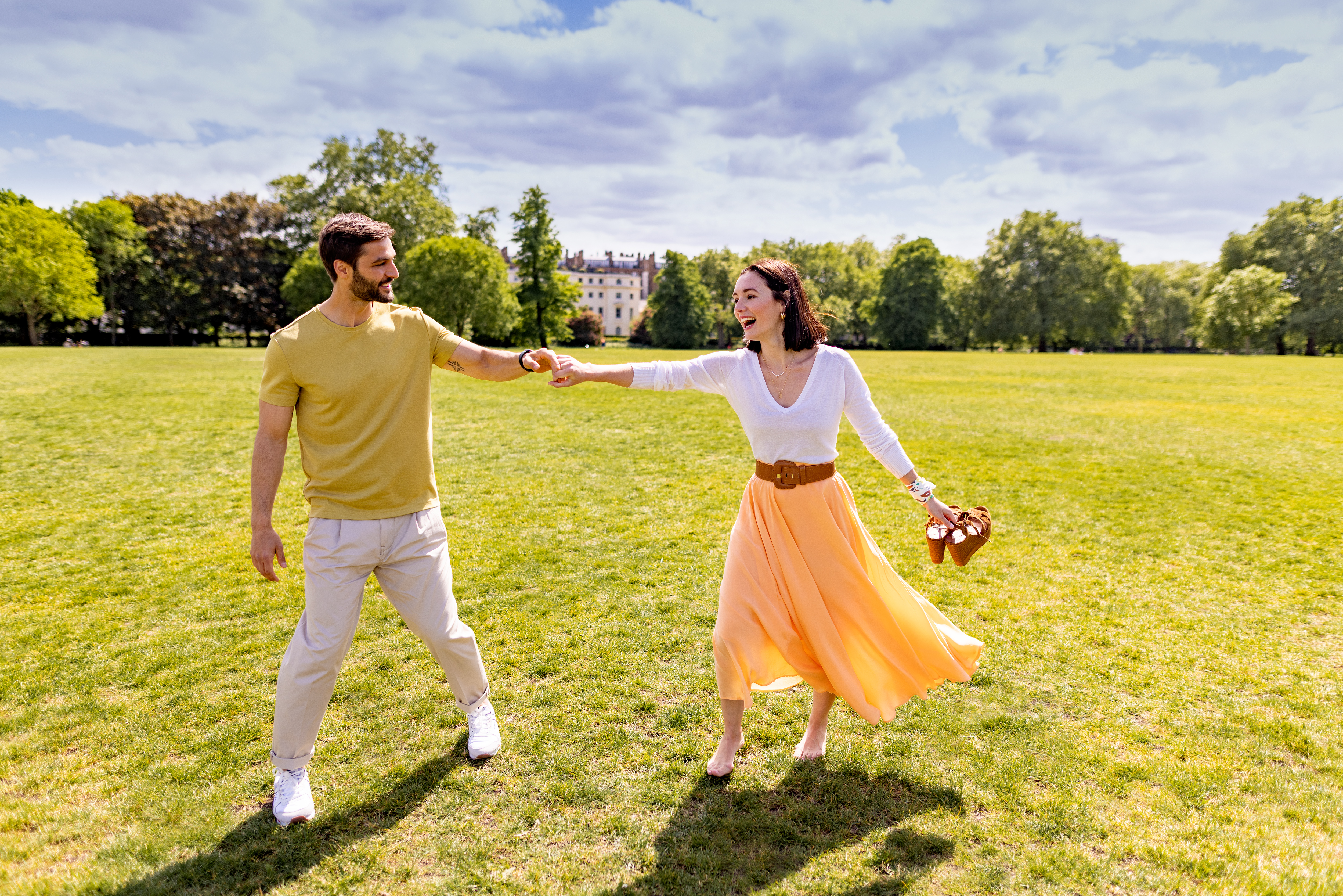 A man and a woman walk together, hand in hand, through a park.