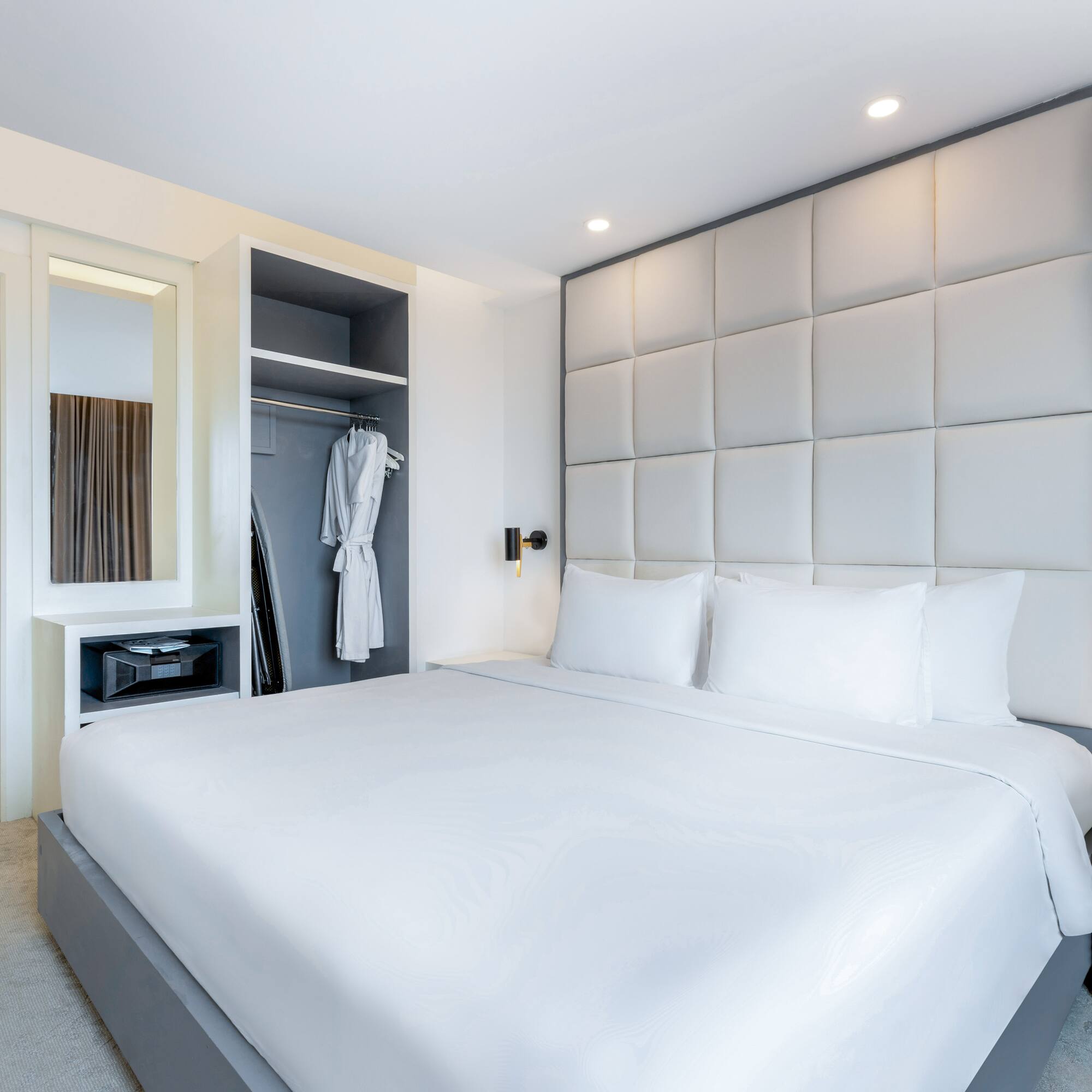 a bed with white sheets and a white robe on a closet