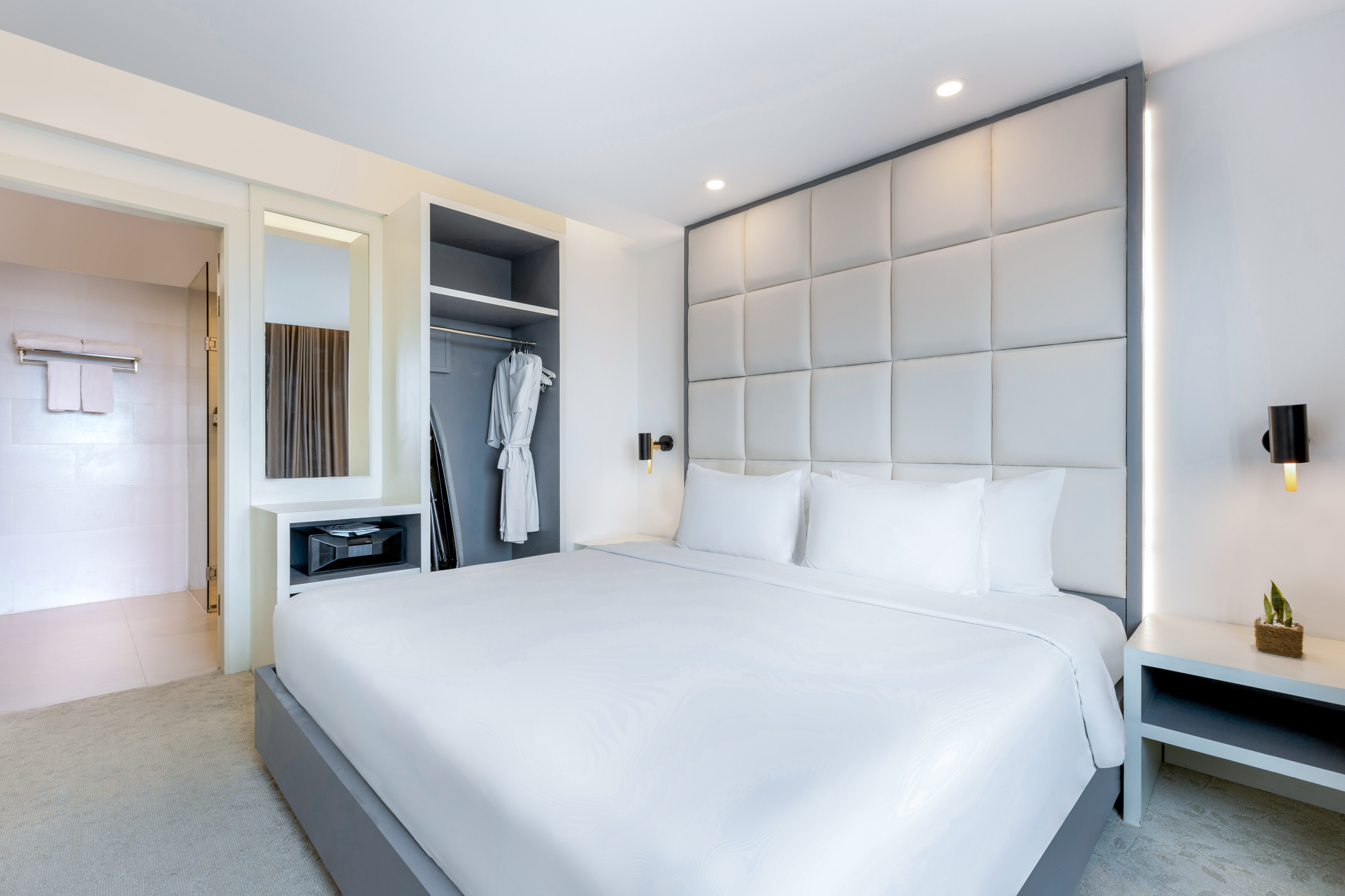 Modern hotel room with white king bed, padded headboard, and built-in closet.