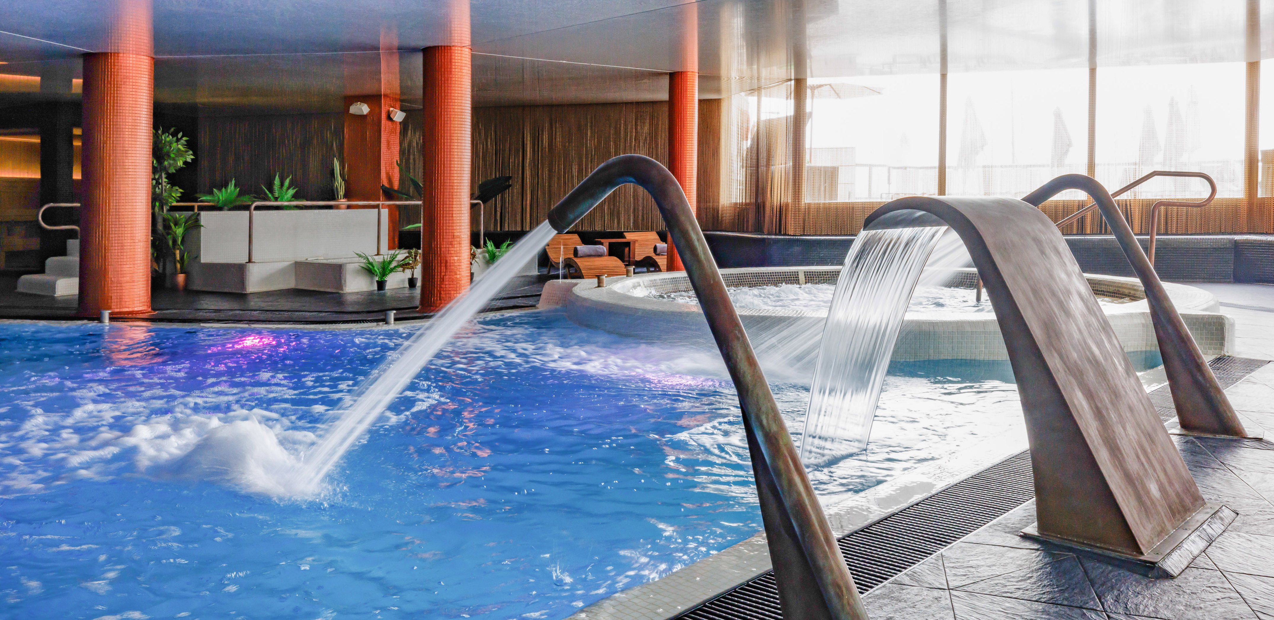 Indoor spa pool with water jets, waterfall, and adjacent hot tub.