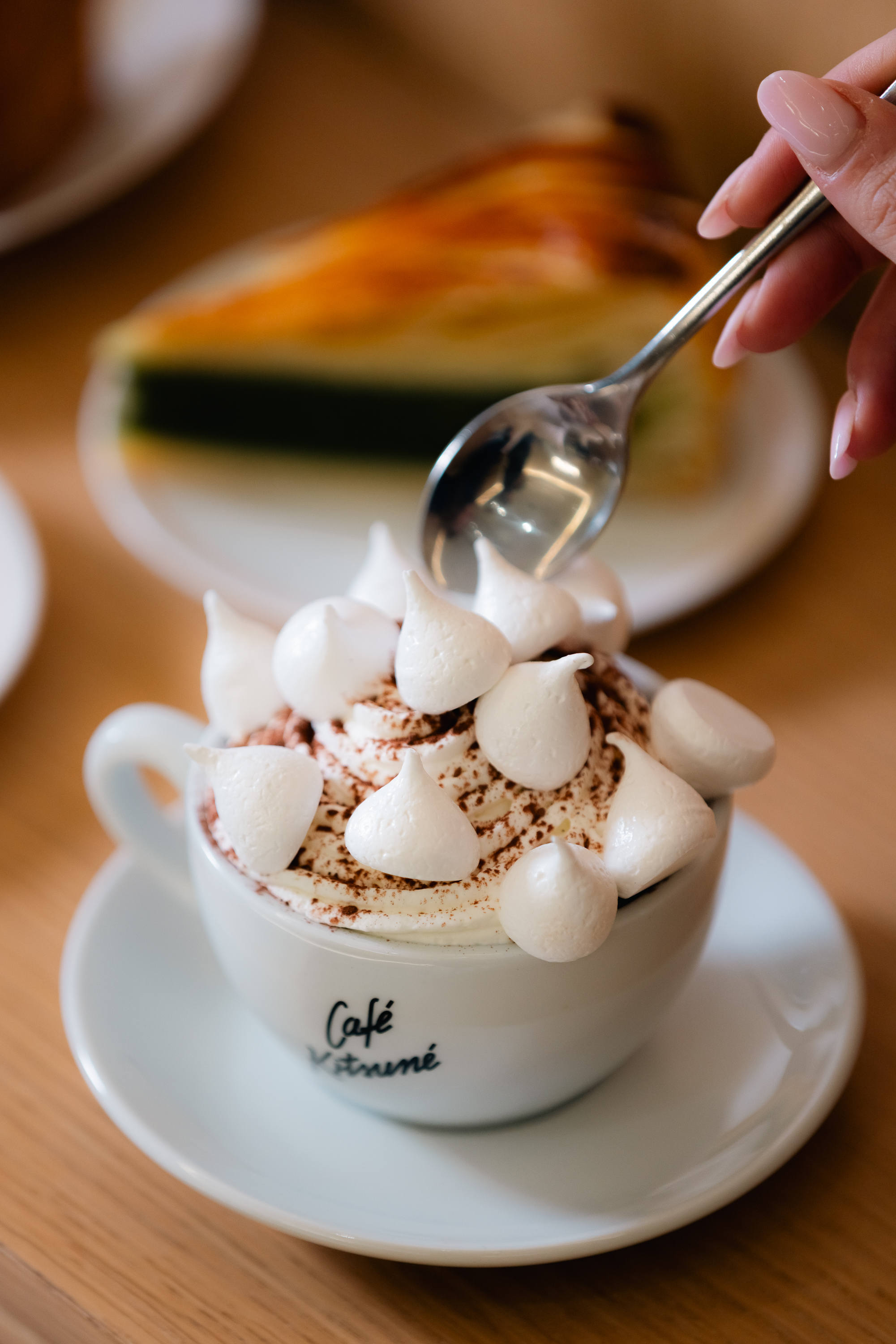 Cafe Kitsuné coffee with whipped cream, meringues, cocoa, and hand with spoon.